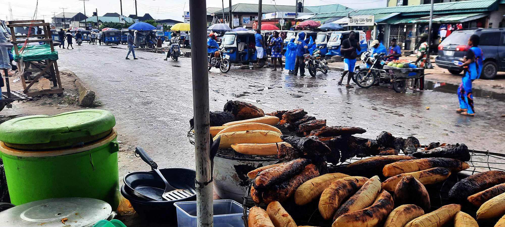 Et travelt veikryss i den nigerianske byen Warri hvor det står mange blå TukTuker og ange mennesker går forbi. 