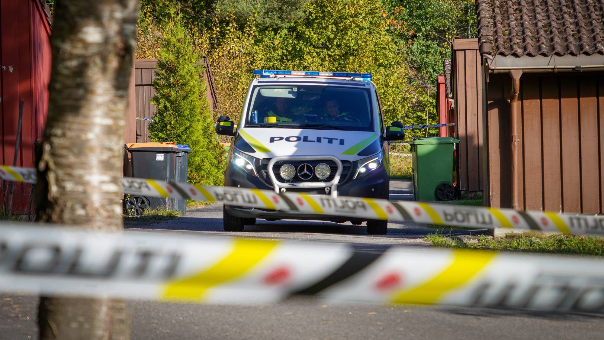 En politibil står mellom flere små bygninger. I forgrunnen er det satt opp sperrebånd.