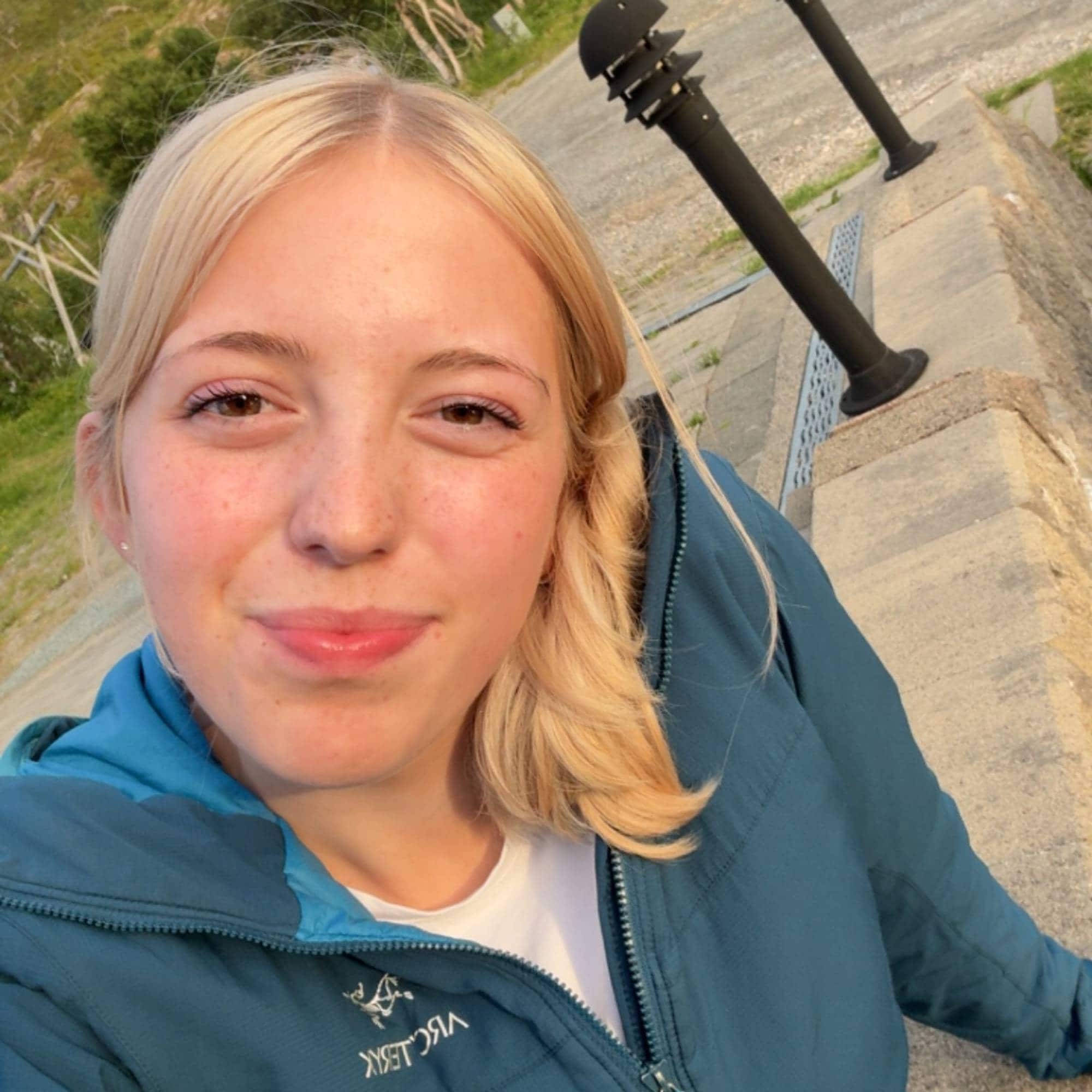 Ei jente med blondt hår smiler i kamera, har på seg blå jakke.
