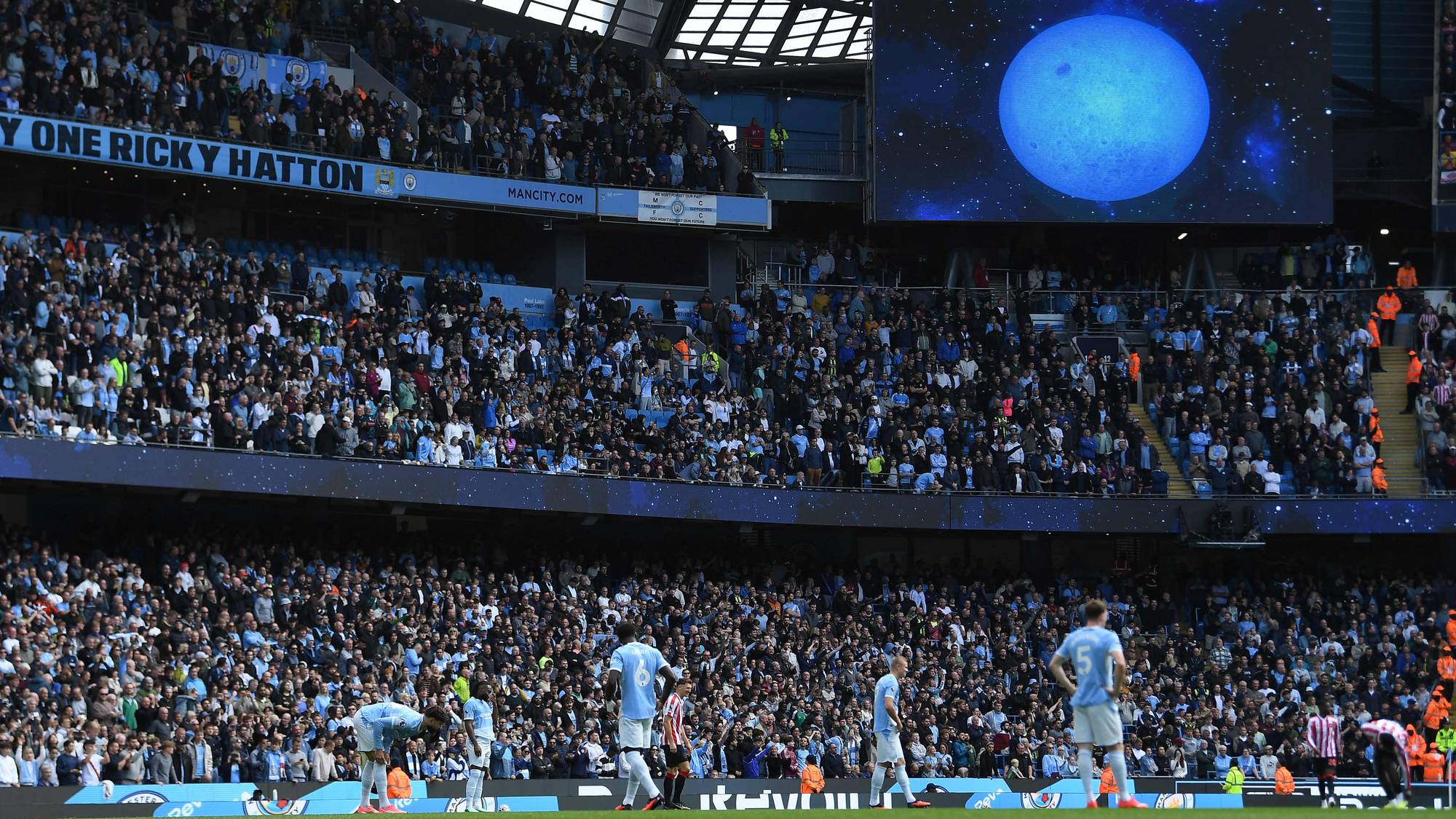 Fylte tribuner på Etihad Stadium med en storskjerm som viser en blå måne. (Bildebeskrivelsen er laget av en KI-tjeneste)