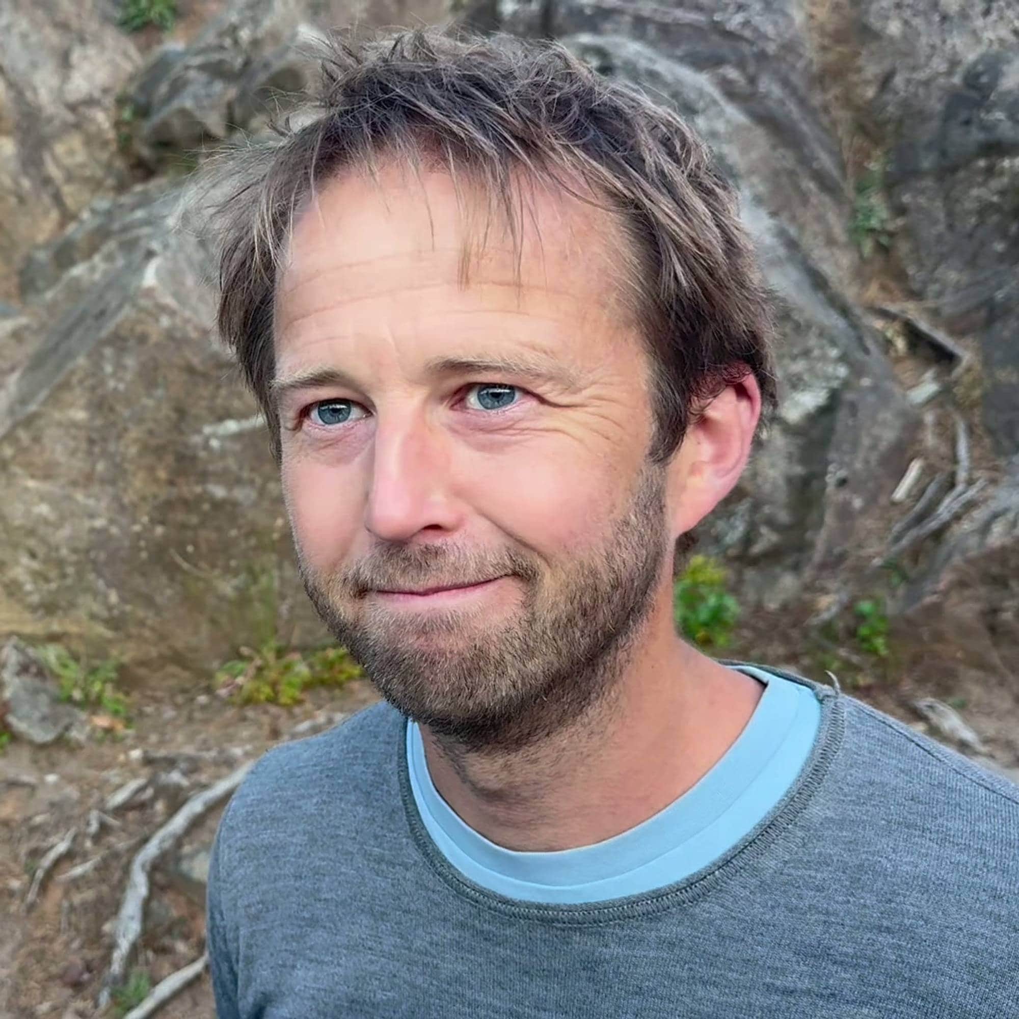 Portrett av en mann med skjegg foran en fjellvegg. (Bildebeskrivelsen er laget av en KI-tjeneste)