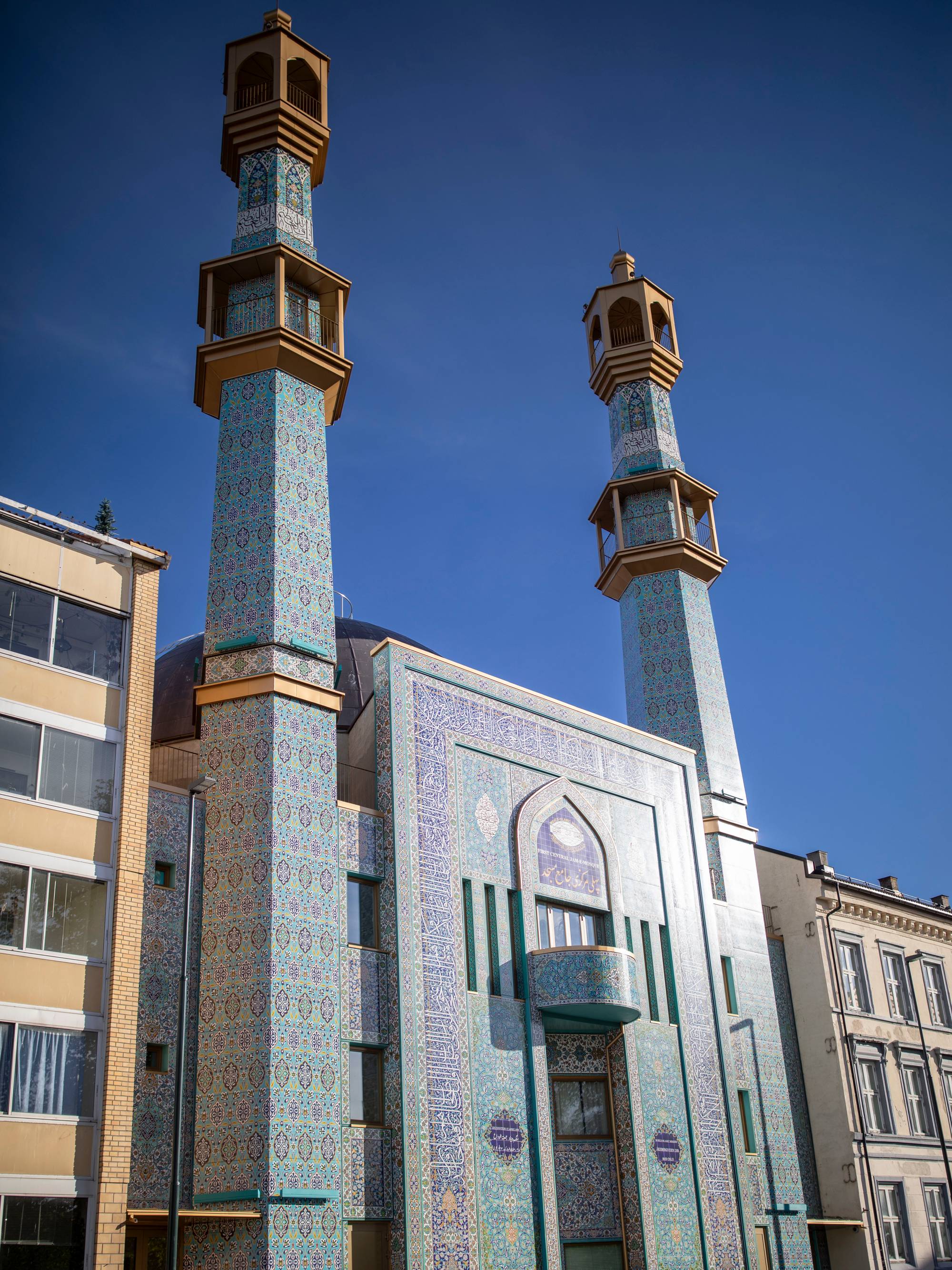 Moské med to minareter og blå flisdekor i en bygate under en klar blå himmel. (Bildebeskrivelsen er laget av en KI-tjeneste)