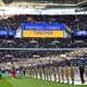 JUSTIN TALLIS / AFP / NTB En stor folkemengde fyller Wembley Stadium, hvor flagg og bannere heises. På banen står en gruppe soldater i uniform, mens en person i rød drakt er synlig nær fronten. Det vises også et stort skilt med teksten "FOOTBALL STANDS TOGETHER." Omgivelsene har et festlig preg, med fans som heier og støtter sine lag. (Bildebeskrivelsen er laget av en KI-tjeneste)