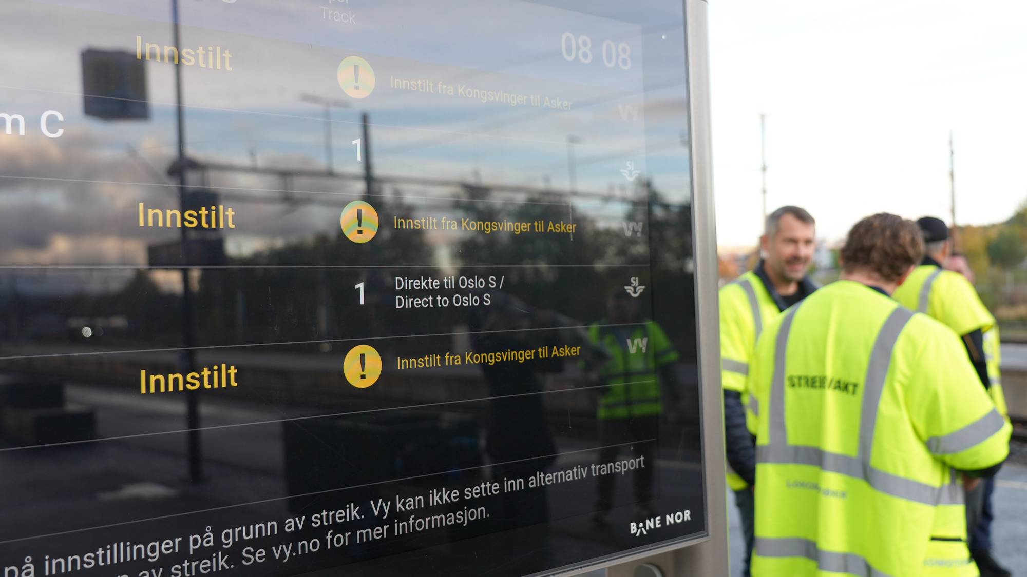 Informasjonstavle viser toginnstillinger på grunn av streik, med togpersonell i refleksvester.