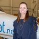 Pilot Flight Academy En kvinne med mørkt hår, i blå bluse foran et fly fra Pilot Flight Academy.