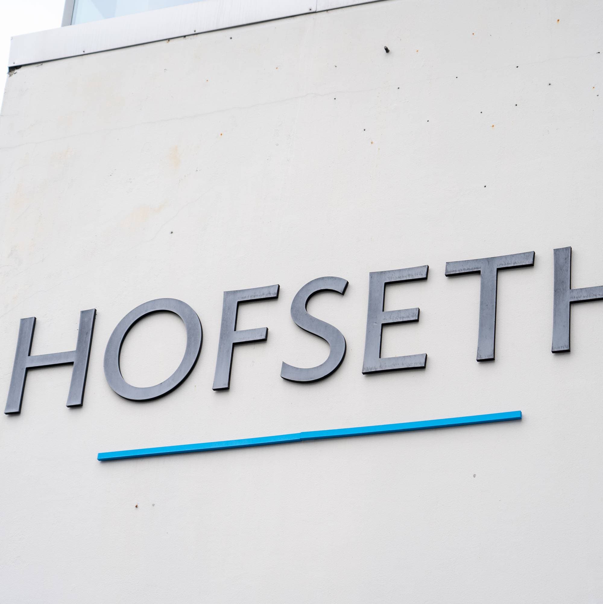 Navnet Hofseth montert som store bokstaver på en lys betongvegg. (Bildebeskrivelsen er laget av en KI-tjeneste)