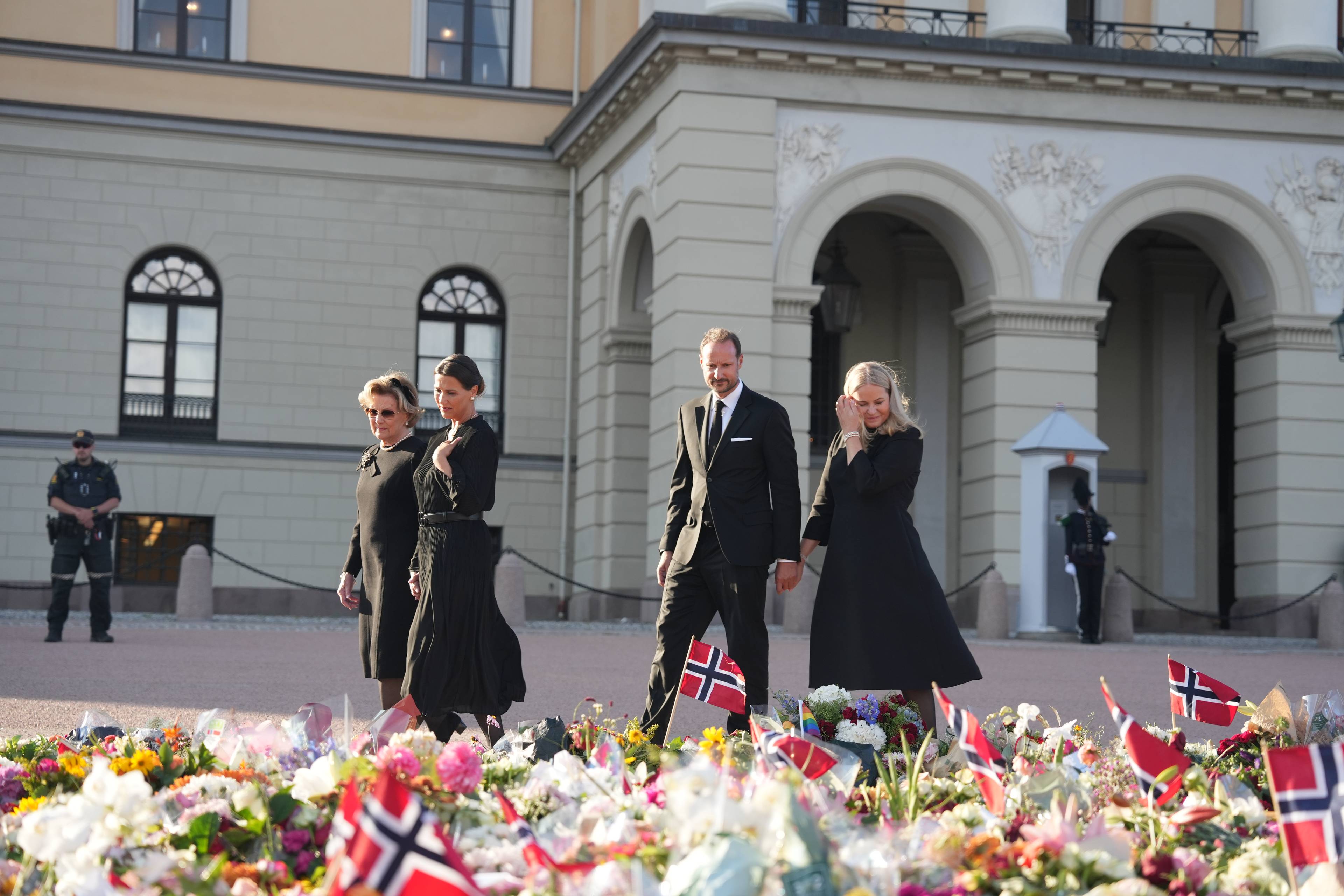 Dronning Sonja, dronning Mette-Marit, kong Haakon og Mrtha Louise ved blomsterhavet. (Bildebeskrivelsen er laget av en KI-tjeneste)