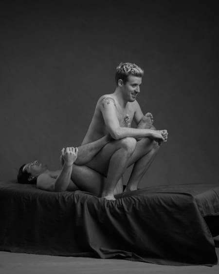 En ung mann med mørkt hår ligger på ryggen og sprer beina. En blond mann sitter med ryggen mot ham, mellom beina til den andre. Begge er nakne, men ingen kjønnsorganer er synlige.