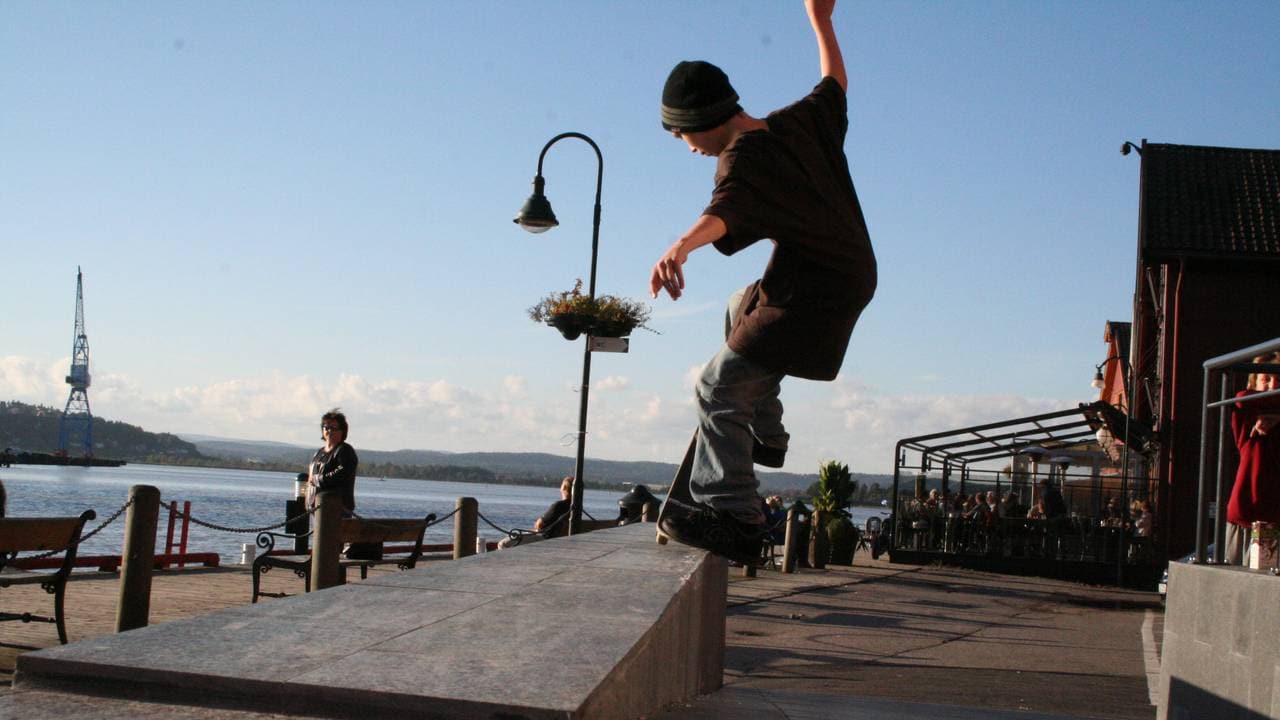 En ung Einar Andrésen skater på brygga i Tønsberg. En dame i bakgrunnen ser på ham.