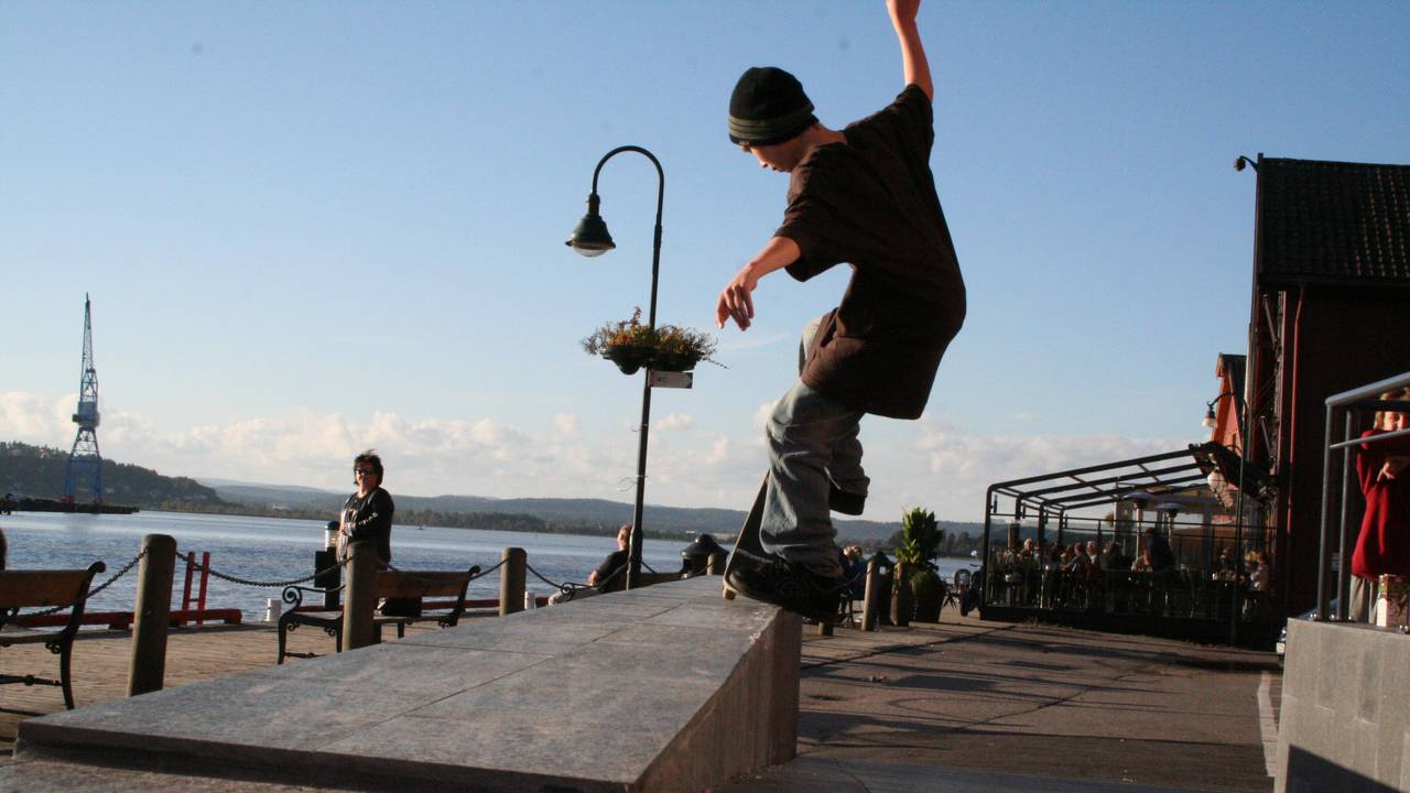 En ung Einar Andrésen skater på brygga i Tønsberg. En dame i bakgrunnen ser på ham.