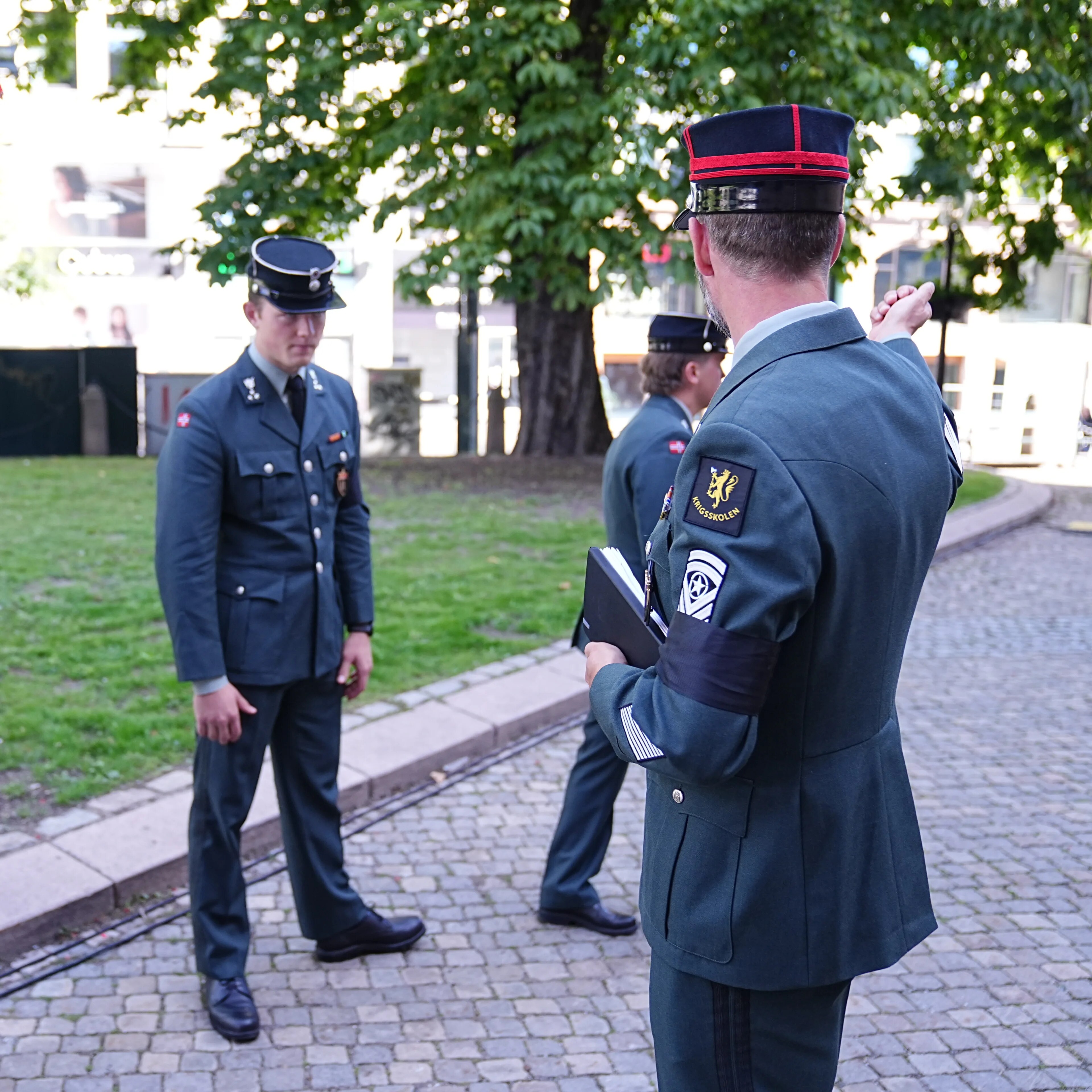 Soldater i uniform står utendørs i en park og samtaler. n peker mens andre lytter. (Bildebeskrivelsen er laget av en KI-tjeneste)