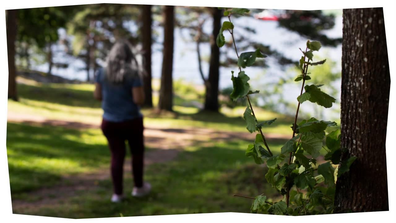 Thea går på en skogsti. Det er sol og grønt ute, i bakgrunnen skimtes et vann.