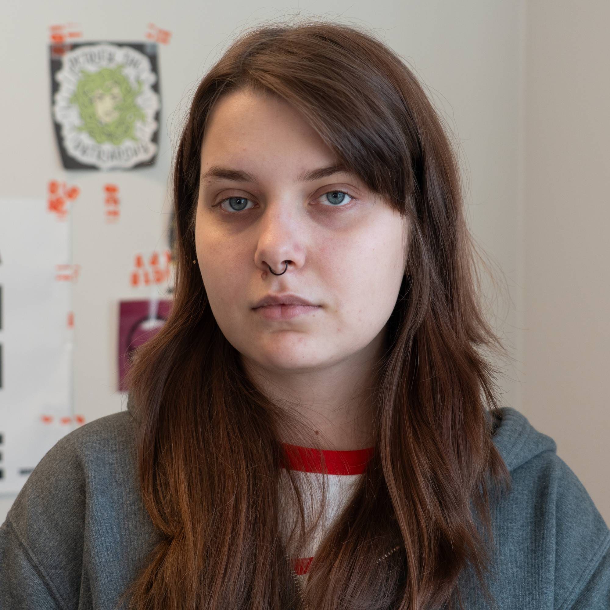 Kvinne med langt brunt hår foran en vegg med plakater med kyrillisk skrift. (Bildebeskrivelsen er laget av en KI-tjeneste)