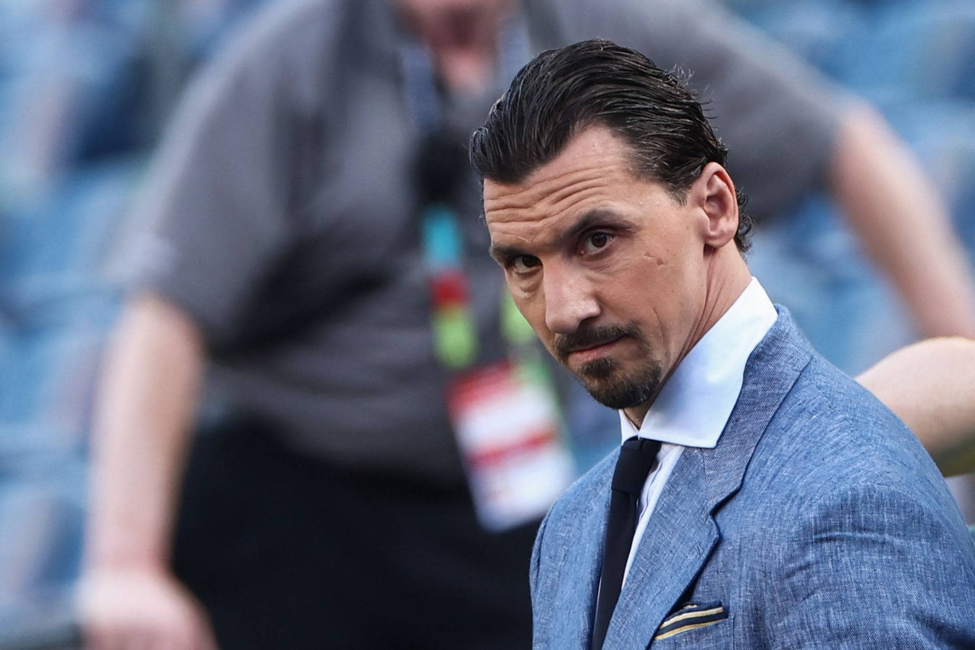 Zlatan Ibrahimovic i blå dressjakke og slips, sett fra siden. Bakgrunnen er uklar. (Bildebeskrivelsen er laget av en KI-tjeneste)