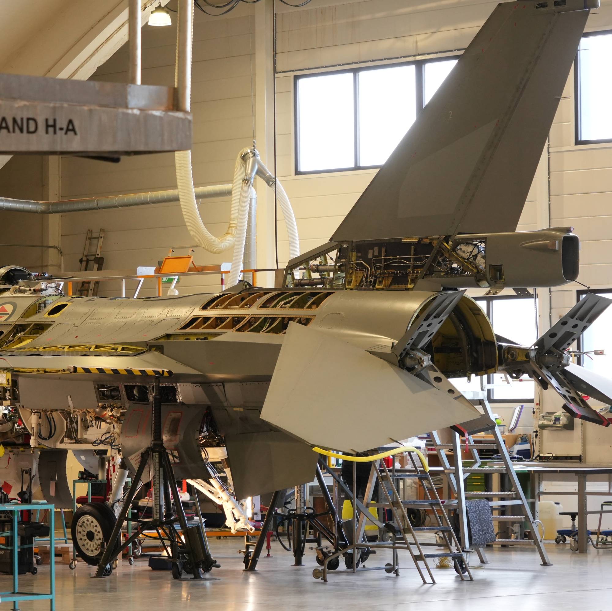 Et F-16-jagerfly sees på verktsted i Bodø. Flyet har tatt av flere ulike paneler som gjør at man ser inn bak flykroppen.