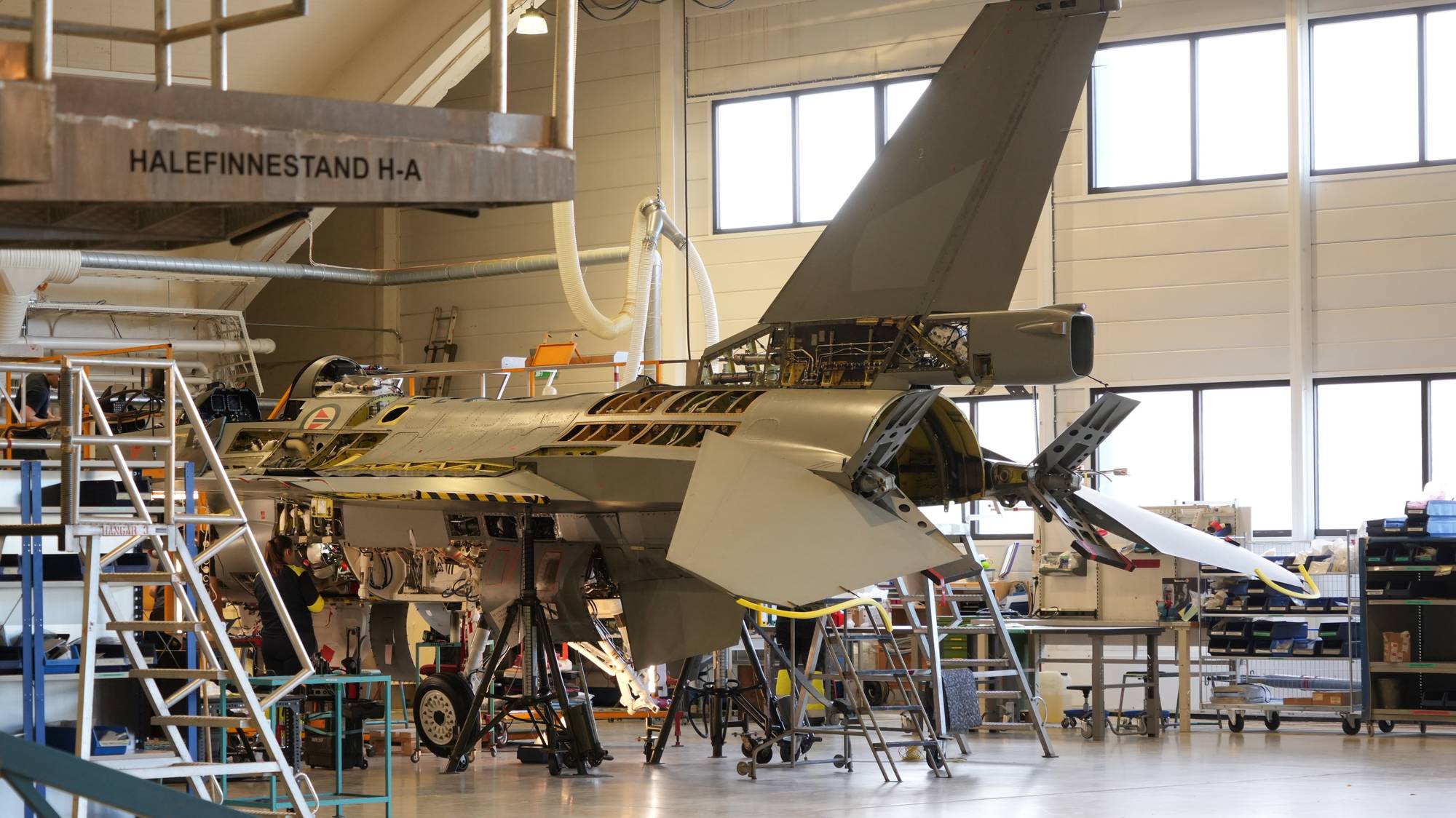 Et F-16-jagerfly sees på verktsted i Bodø. Flyet har tatt av flere ulike paneler som gjør at man ser inn bak flykroppen.