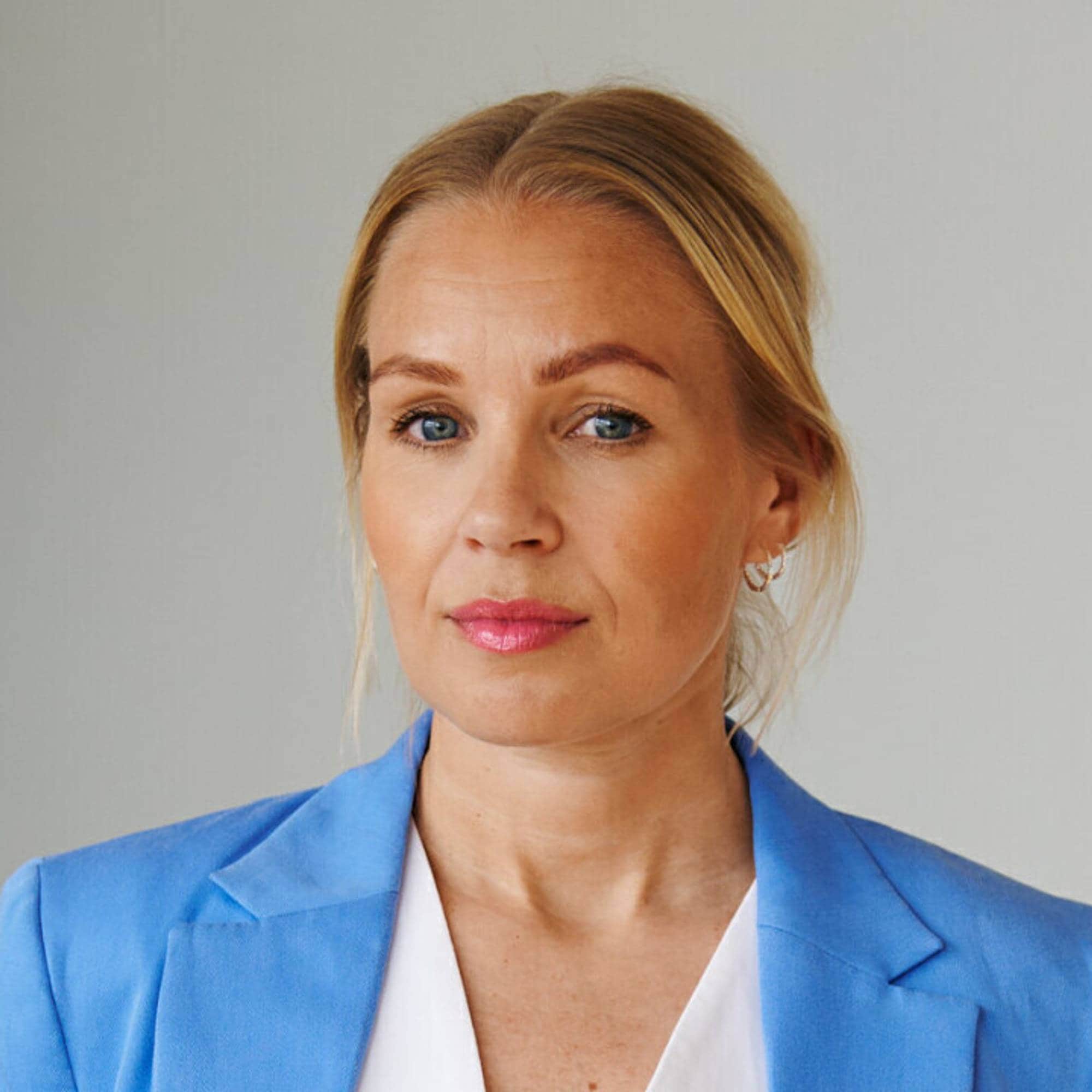Sigri smiler med blå blazer og hvit t-skjorte. Hun har hestehale og ser alvorlig ut. 