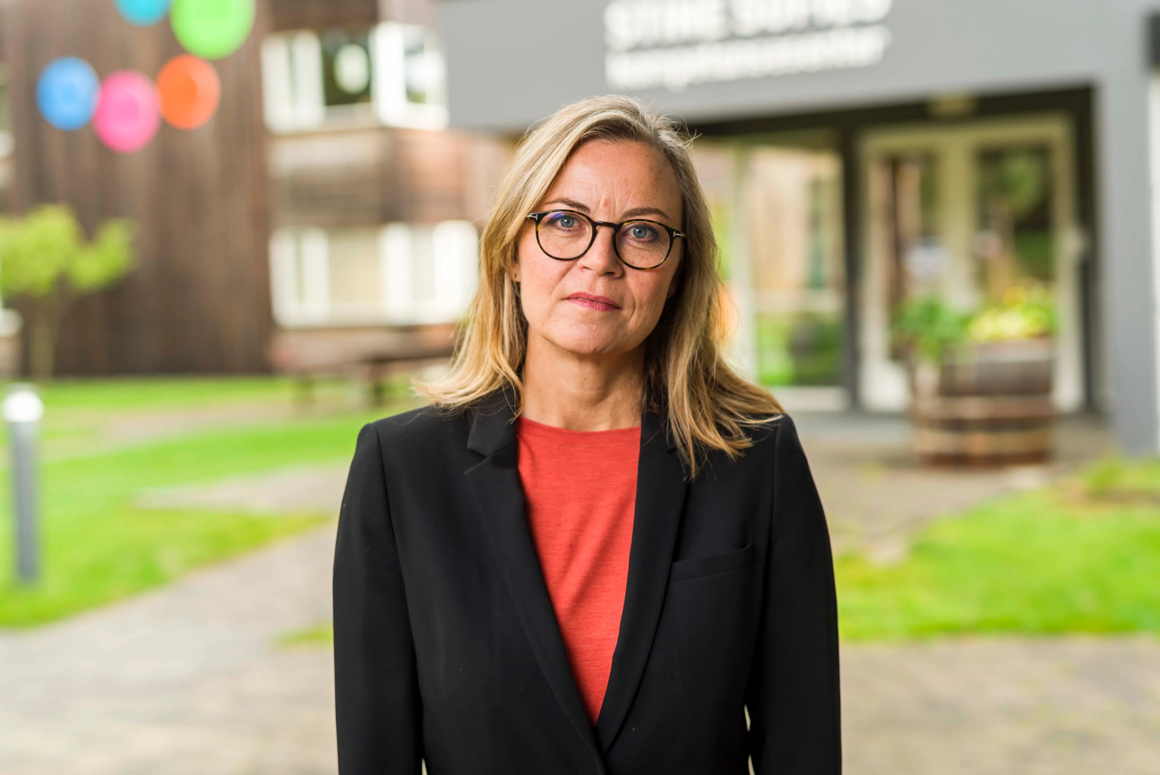 En kvinne som bruker briller. Hun har på seg rød t-skjorte og svart blazer.