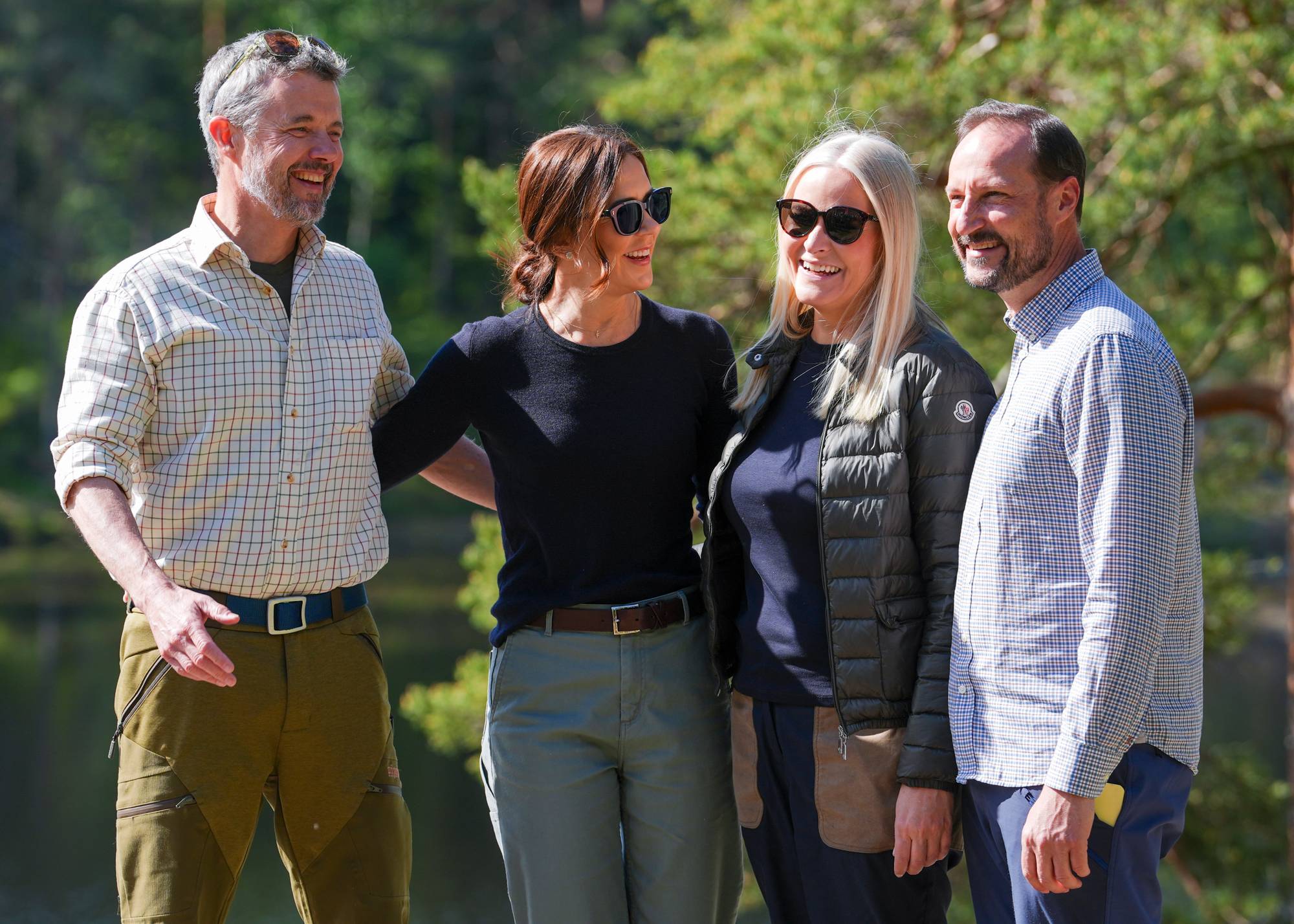 Kong Frederik, dronning Mary, kronprins Haakon og kronprinsesse Mette-Marit holder rundt hverandre og smiler mens de fotograferes ved Ulsrudvannet i Oslo