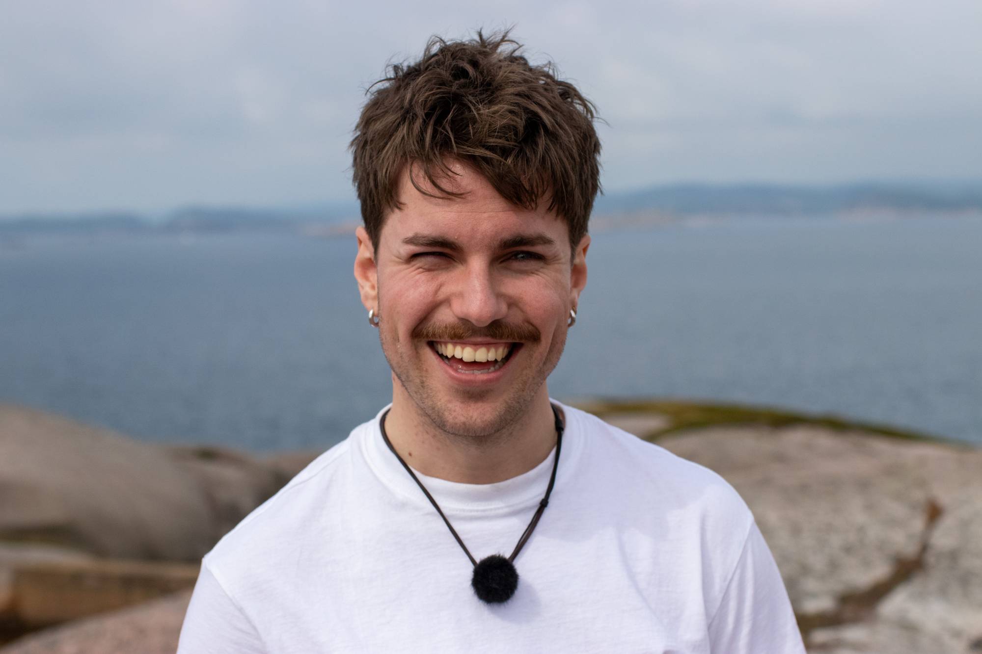 en mann som smiler med vann i bakgrunnen