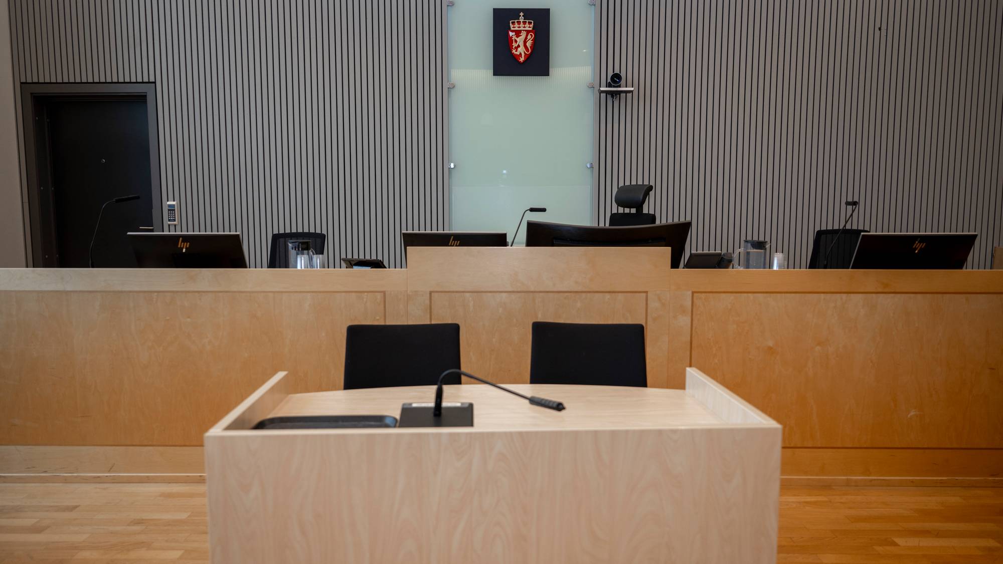 Dommersete i en rettssal med riksvåpenet på veggen bak en trebenk. Et vitnebord står foran. (Bildebeskrivelsen er laget av en KI-tjeneste)