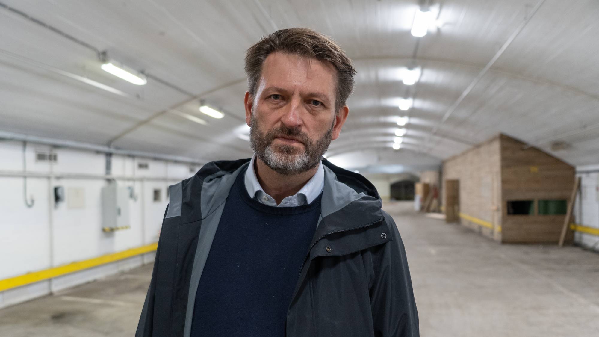 En mann med skjegg står i en langstrakt underjordisk hall med hvite vegger og betonggulv. (Bildebeskrivelsen er laget av en KI-tjeneste)