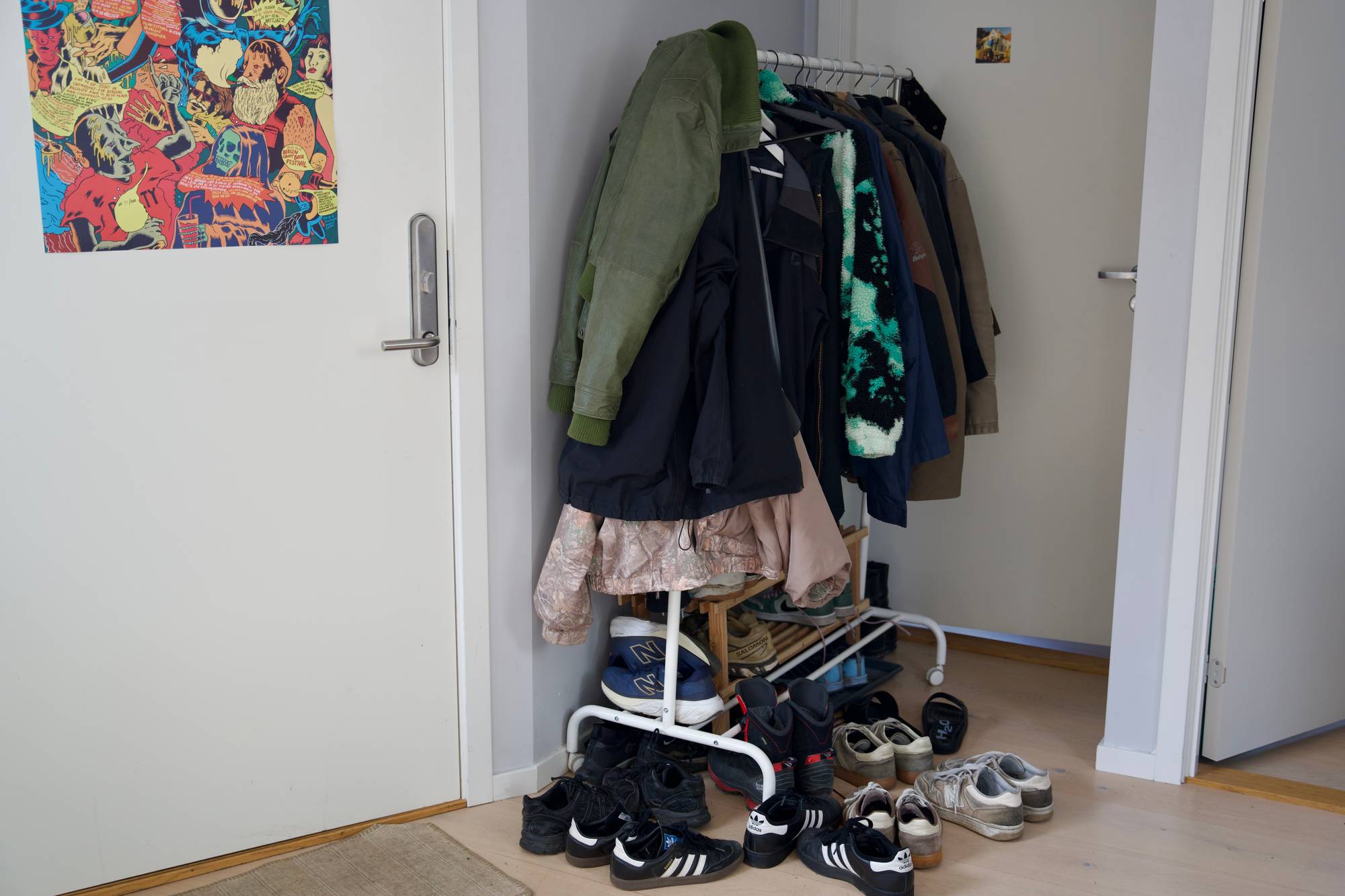 I gangen til kollektivet, står et hvitt klesstativ fylt opp med jakker og skopar. I tillegg står det flere skopar rundt klesstativet. 