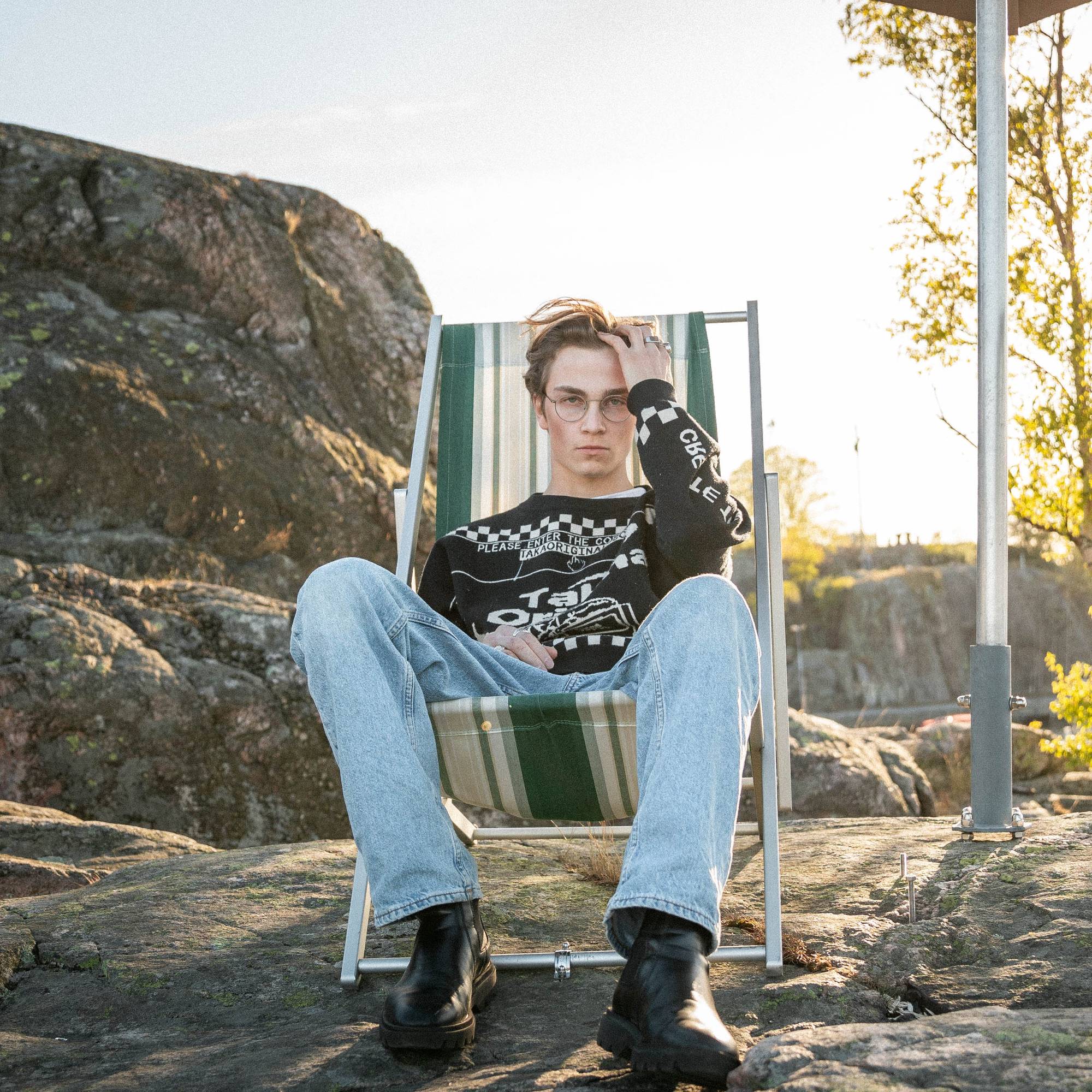 Bilde av skribenten på en fastspent strandstol. Marcus har på seg en svart strikkegenser med blå jeans og svarte boots. Han tar seg i håret. 