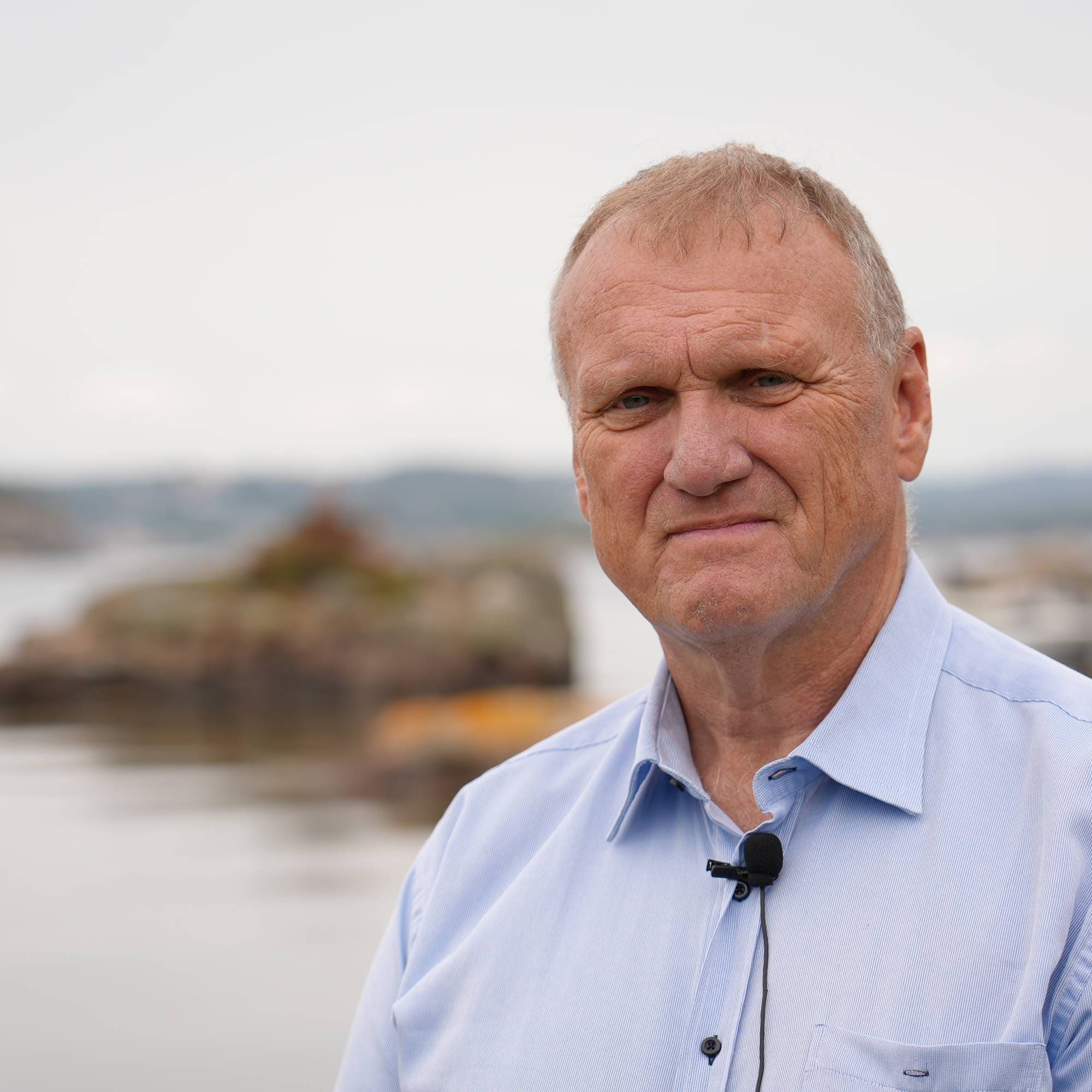 Mann med grått hår og blå skjorte ved vann