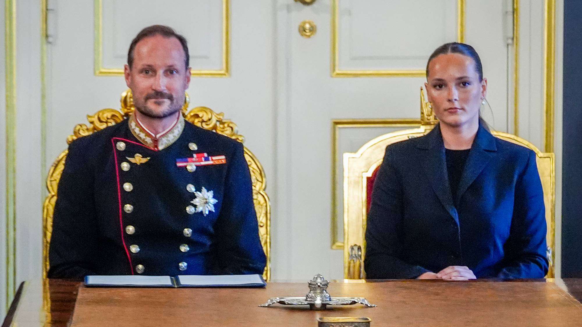 Kronprins Haakon og prinsesse Ingrid Alexandra sitter ved et bord i en formell setting. (Bildebeskrivelsen er laget av en KI-tjeneste)