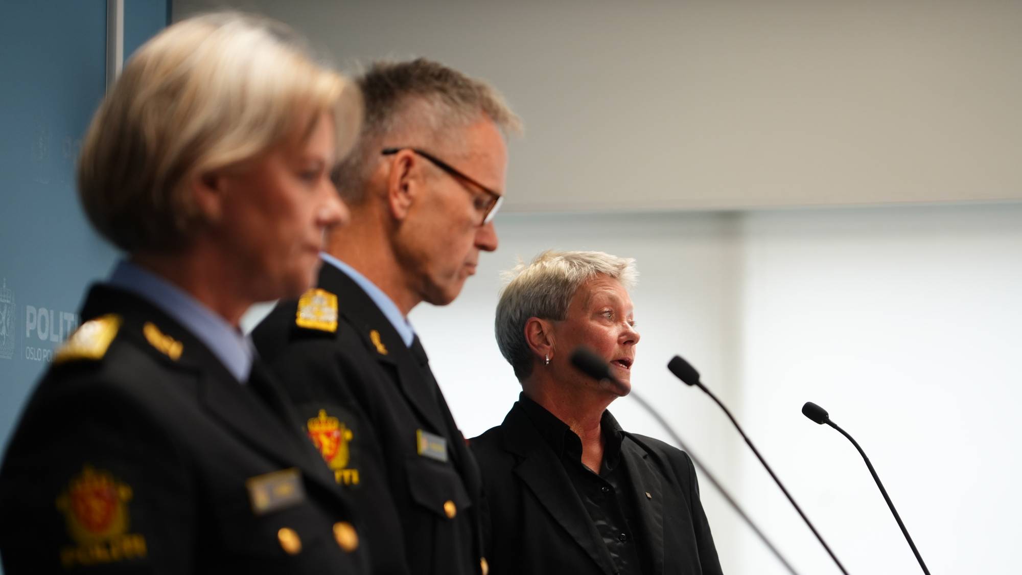 To politiledere og en kvinne i sivil drakt snakker foran mikrofoner på en pressekonferanse. (Bildebeskrivelsen er laget av en KI-tjeneste)