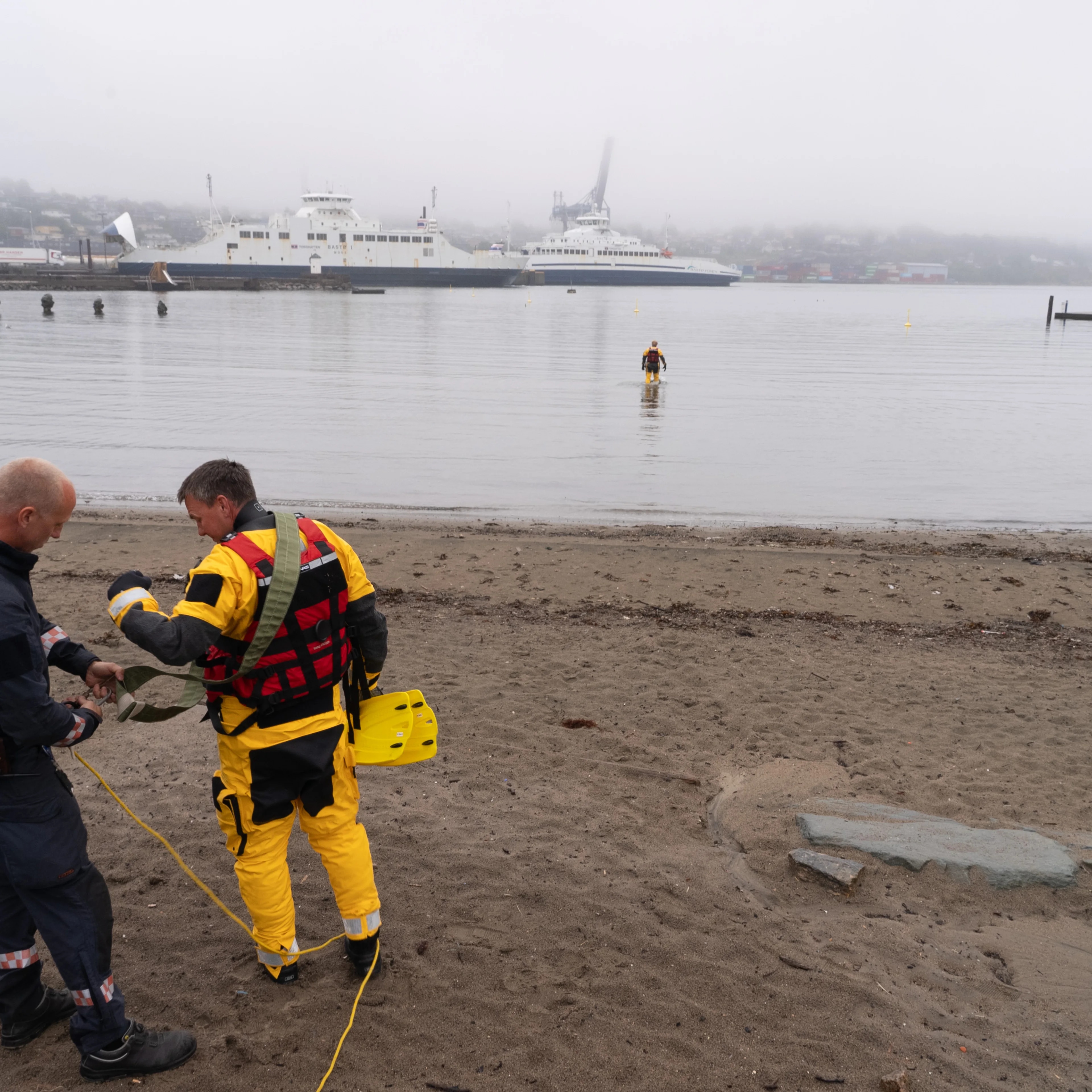 Redningspersonell forbereder en øvelse ved en strand med en båt i bakgrunnen. (Bildebeskrivelsen er laget av en KI-tjeneste)