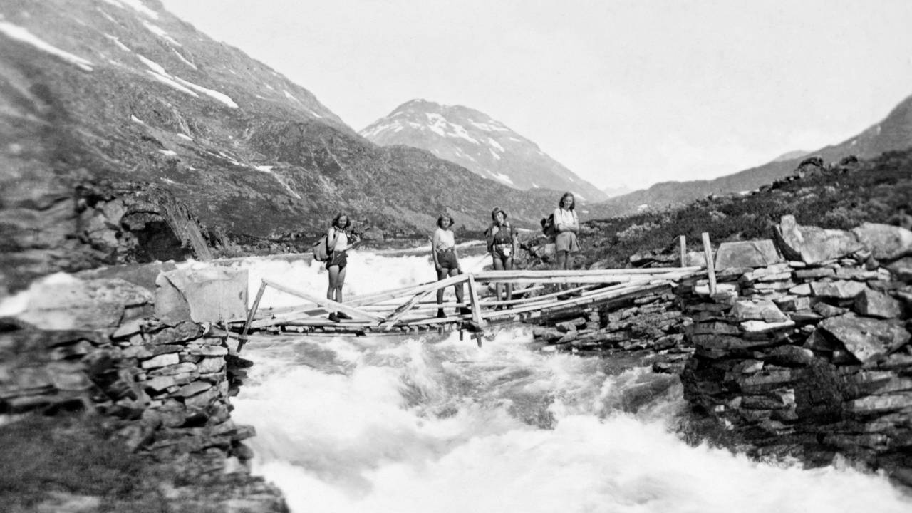 Fire elverumsjenter på fottur i Jotunheimen sommeren 1943. Marie Horst, Mette Grøner, Sosse Nielsen og Putte Høye er fotografert stående på ei enkel trebru over ei kvitskummende elv på vegen mot Skogadalsbøen i Luster i Sogn.