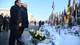 Ukrainas utenriksdepartement / Ukrainas utenriksdepartement To personer står foran et minnesmerke dekket med snø og blomster. De ser mot en rekke flagg som er reist i området. Flere mennesker er samlet i bakgrunnen, og bygninger er synlige langs gaten. Dagen er klar med blå himmel og sollys.