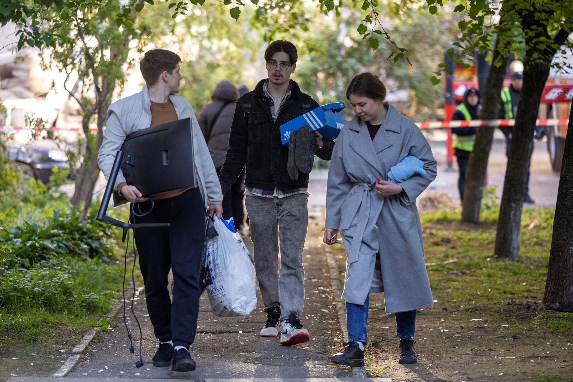 Tre personer går på en gangvei utendørs. En mann bærer en dataskjerm og en plastpose. En annen mann bærer en eske. En kvinne bærer et lyseblått plagg. (Bildebeskrivelsen er laget av en KI-tjeneste)