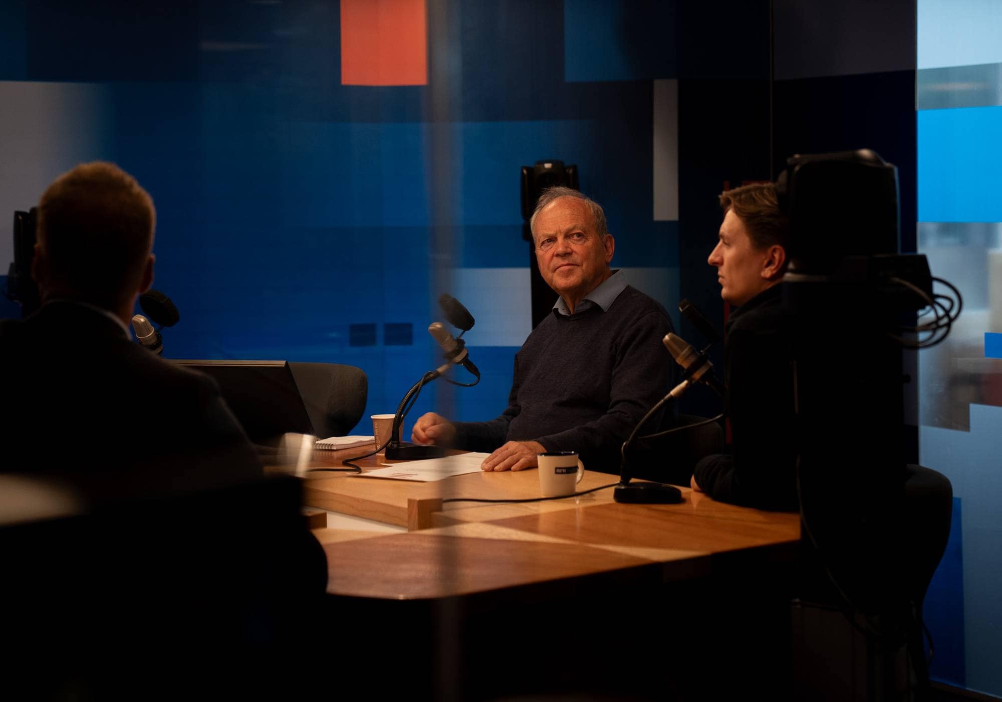 Tre menn og en dame i studio med NRK-farger. 