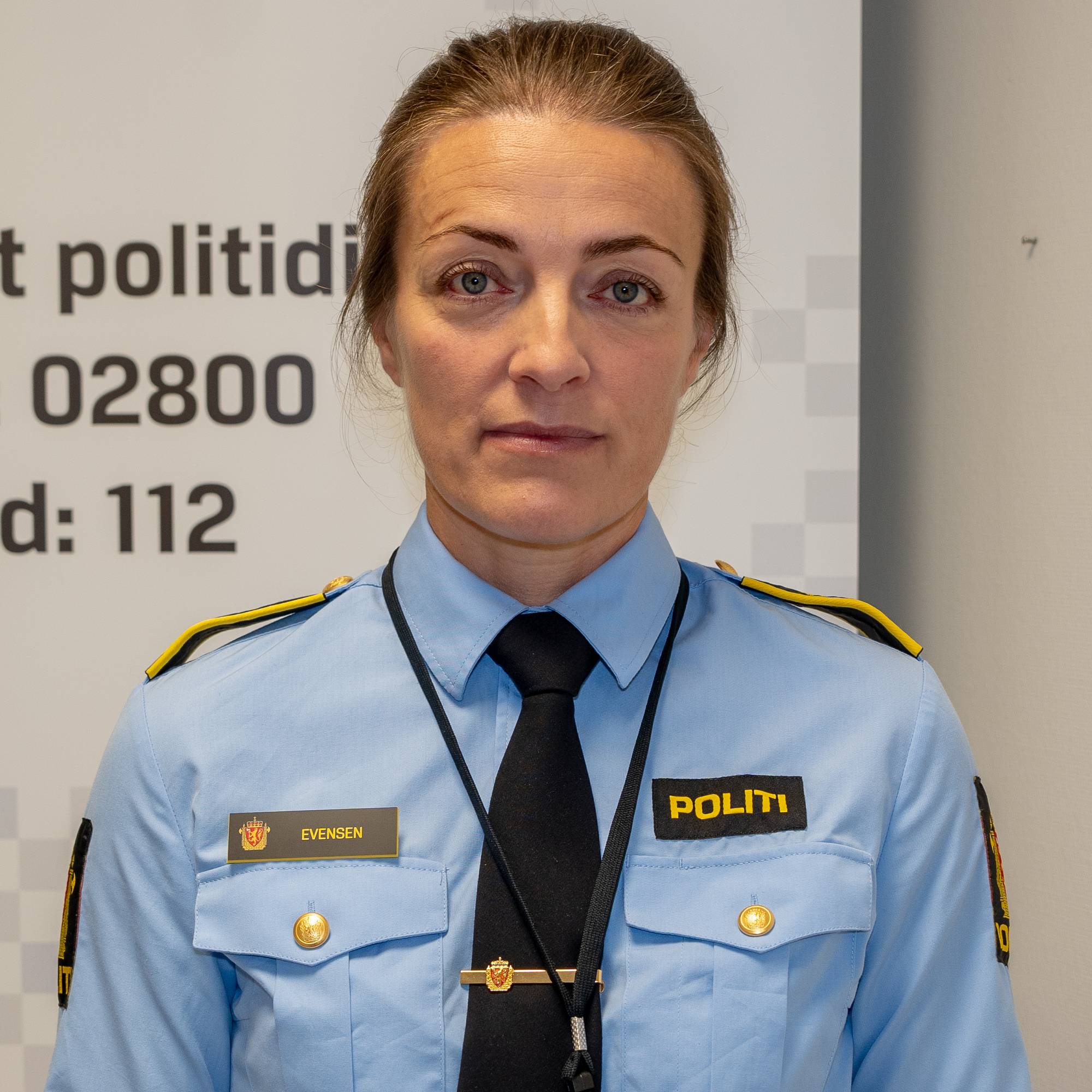 En politikvinne i uniform står foran et skilt fra Politiet. (Bildebeskrivelsen er laget av en KI-tjeneste)