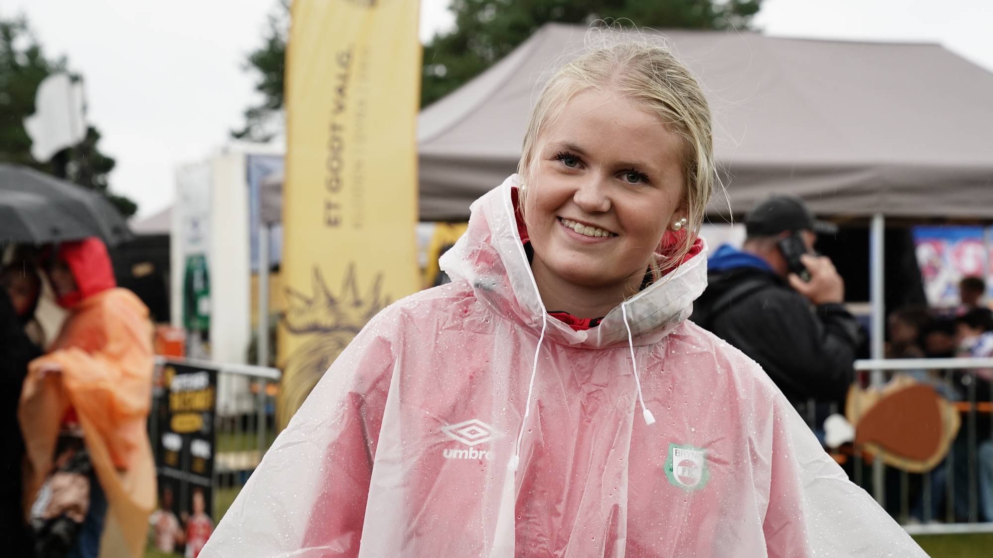 Smilende kvinne i gjennomsiktig regnponcho utendørs. (Bildebeskrivelsen er laget av en KI-tjeneste)