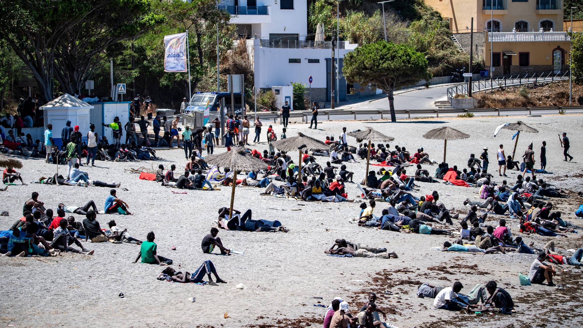 På ei strand sit mange menneske. Dei fleste er mørke i huden og kjem tilsynelatande frå Afrika sør for Sahara.