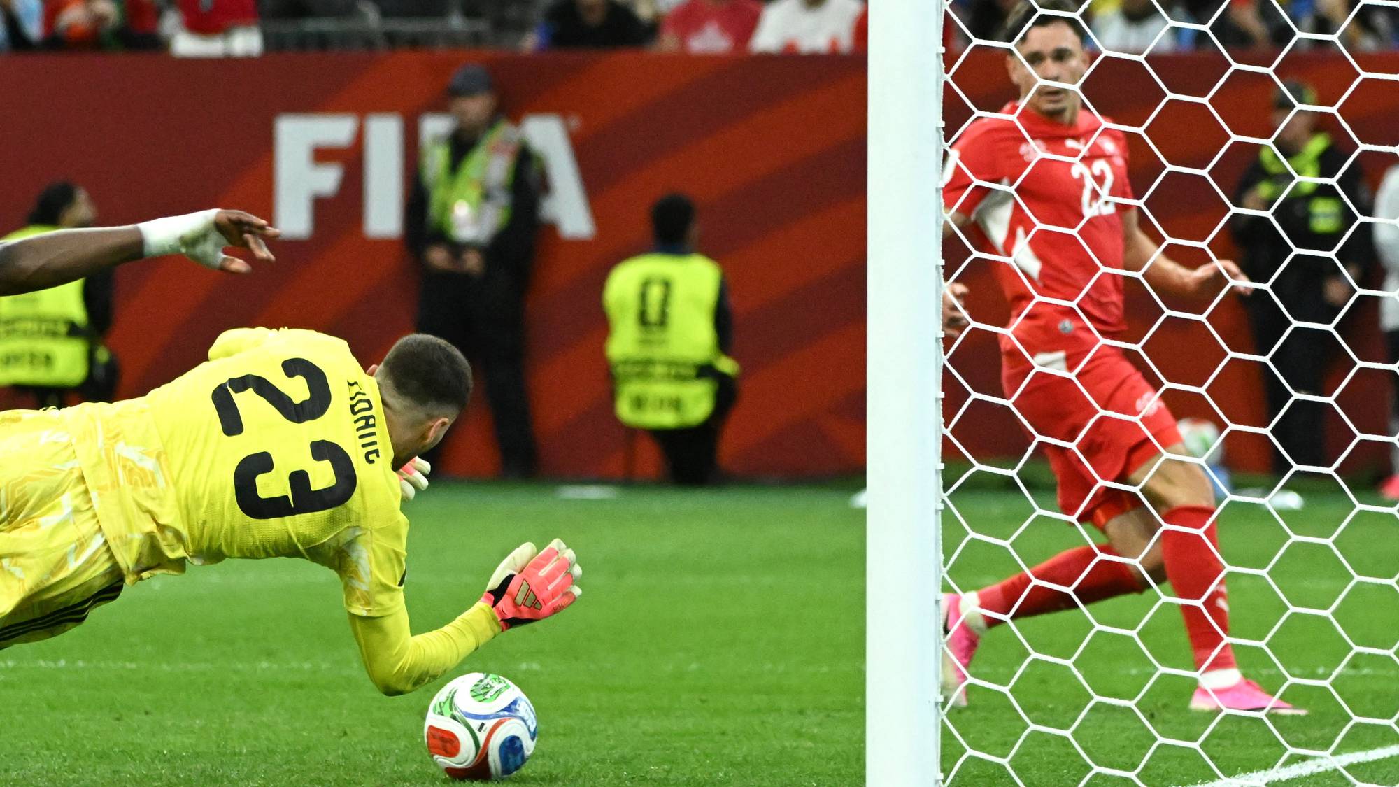 Keeper kaster seg etter en fotball foran et mål, mens en sveitsisk spiller løper i bakgrunnen. (Bildebeskrivelsen er laget av en KI-tjeneste)