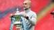 ADRIAN DENNIS / AFP,NTB Pep Guardiola holder FA-cupen. Mannen, som er kledd i en grå genser, holder pokalen med begge hender. I bakgrunnen er tribuner med røde seter. (Bildebeskrivelsen er laget av en KI-tjeneste)
