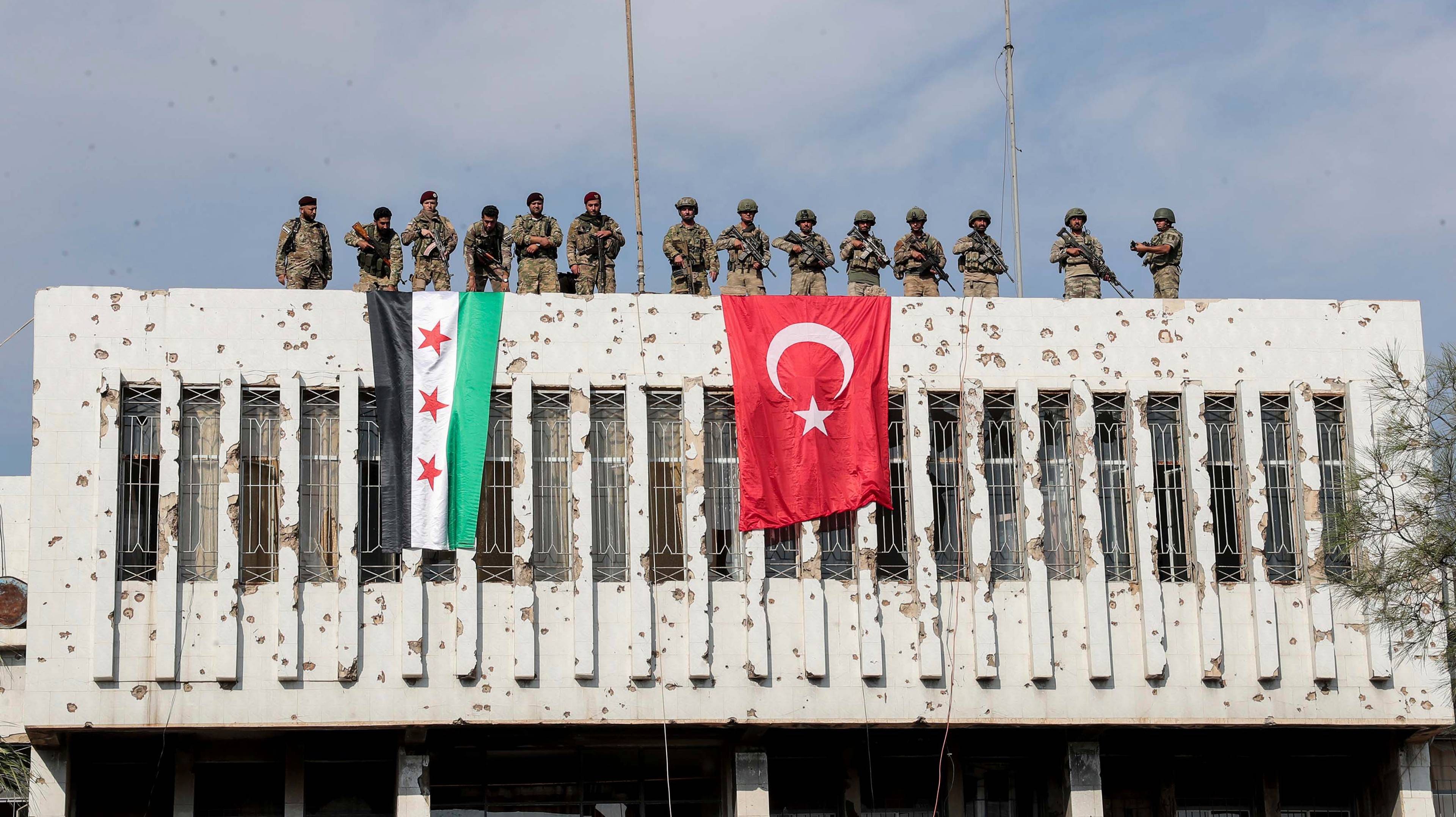 Turkish soldiers, right, and Turkish-backed opposition soldiers stand on top of a building next to their flags in the Syrian city‍ of Ras al Ayn, northeastern Syria, Wednesday, october 23, 2019