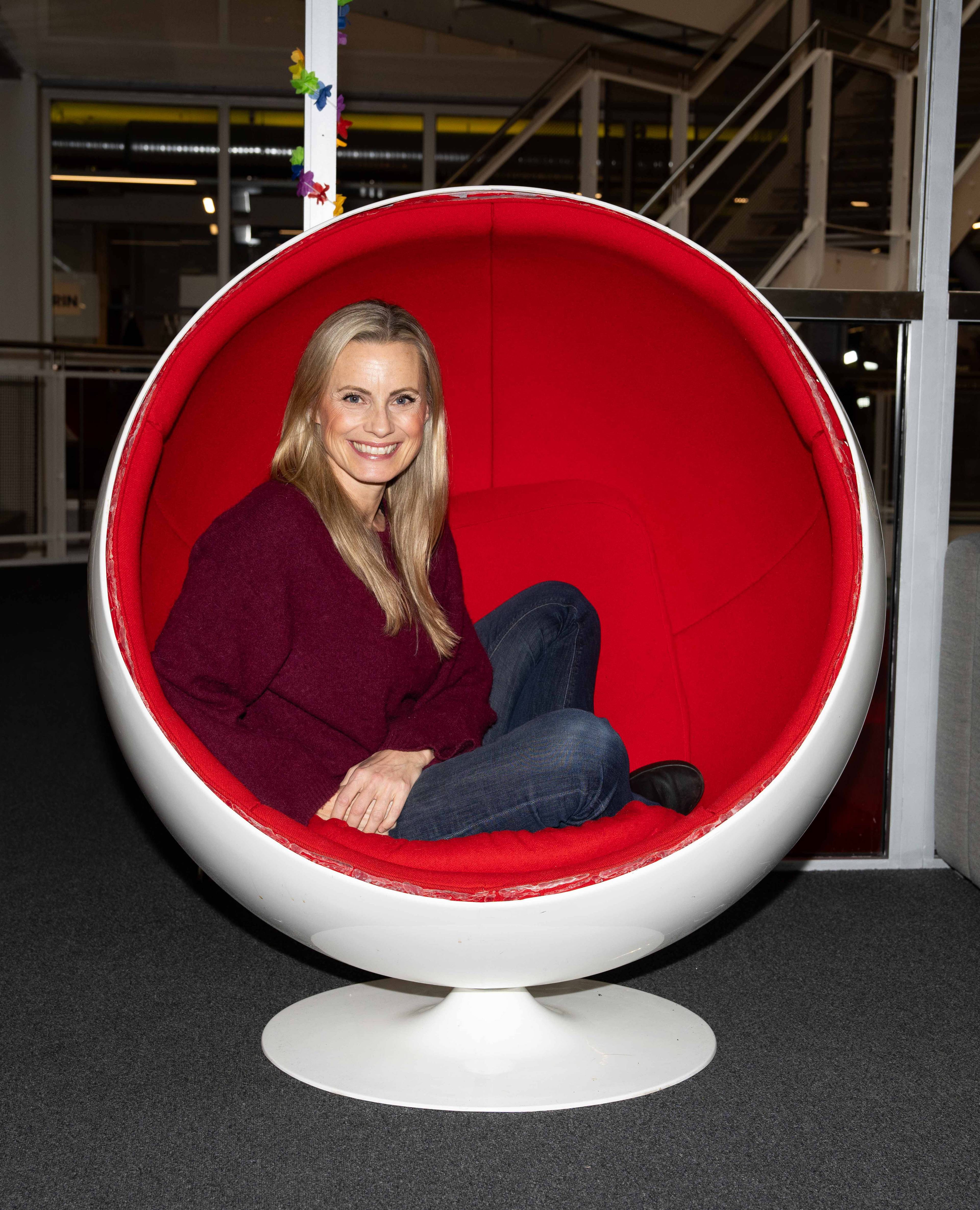 Silje Sandmæl i en rund rød og hvit sofastol. Hun smiler og ser i kamera.