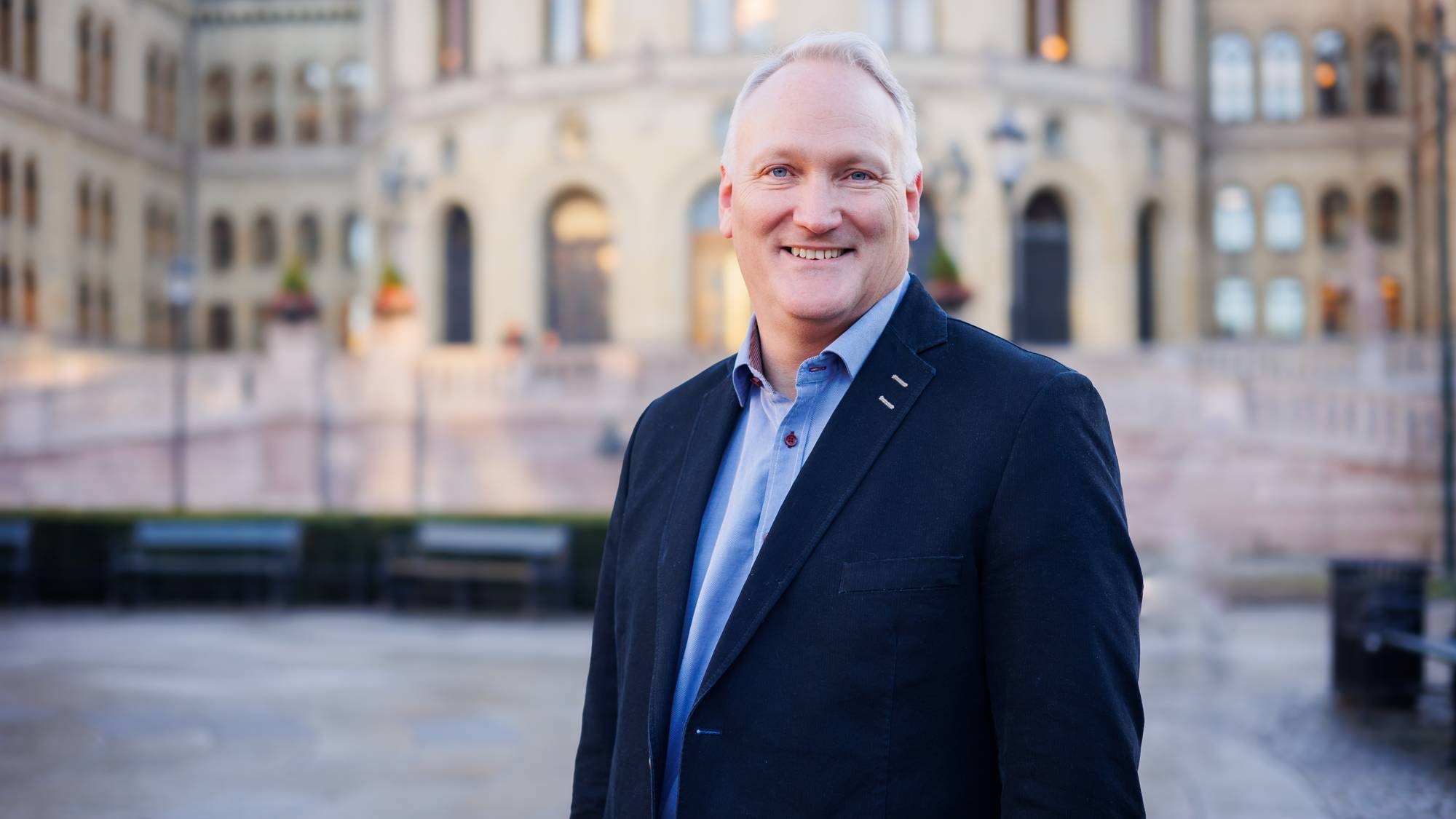 Mann står foran stortinget i dress