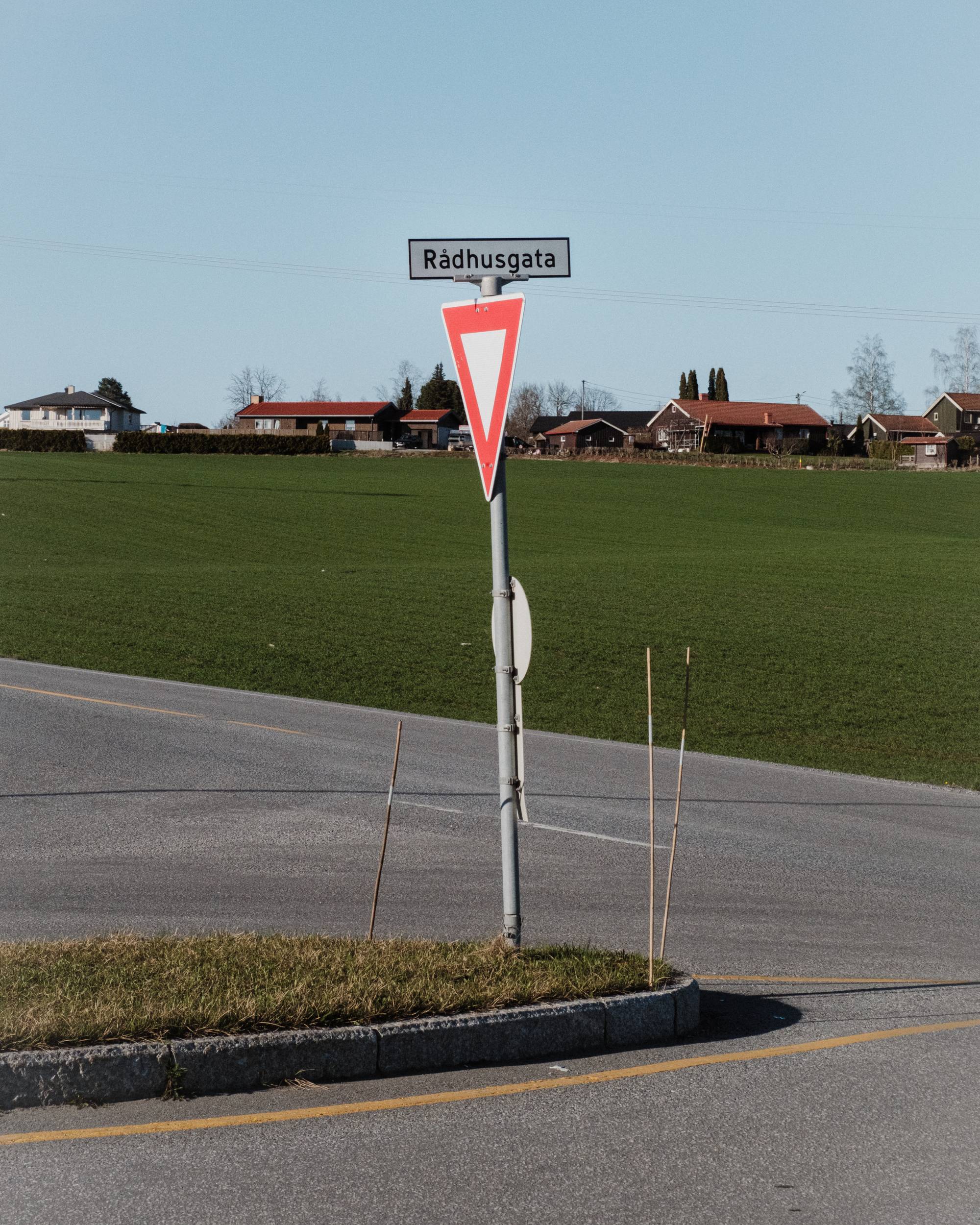 Et vikepliktskilt med skilting mot Rådhusgata festet over står på en vei foran en åker