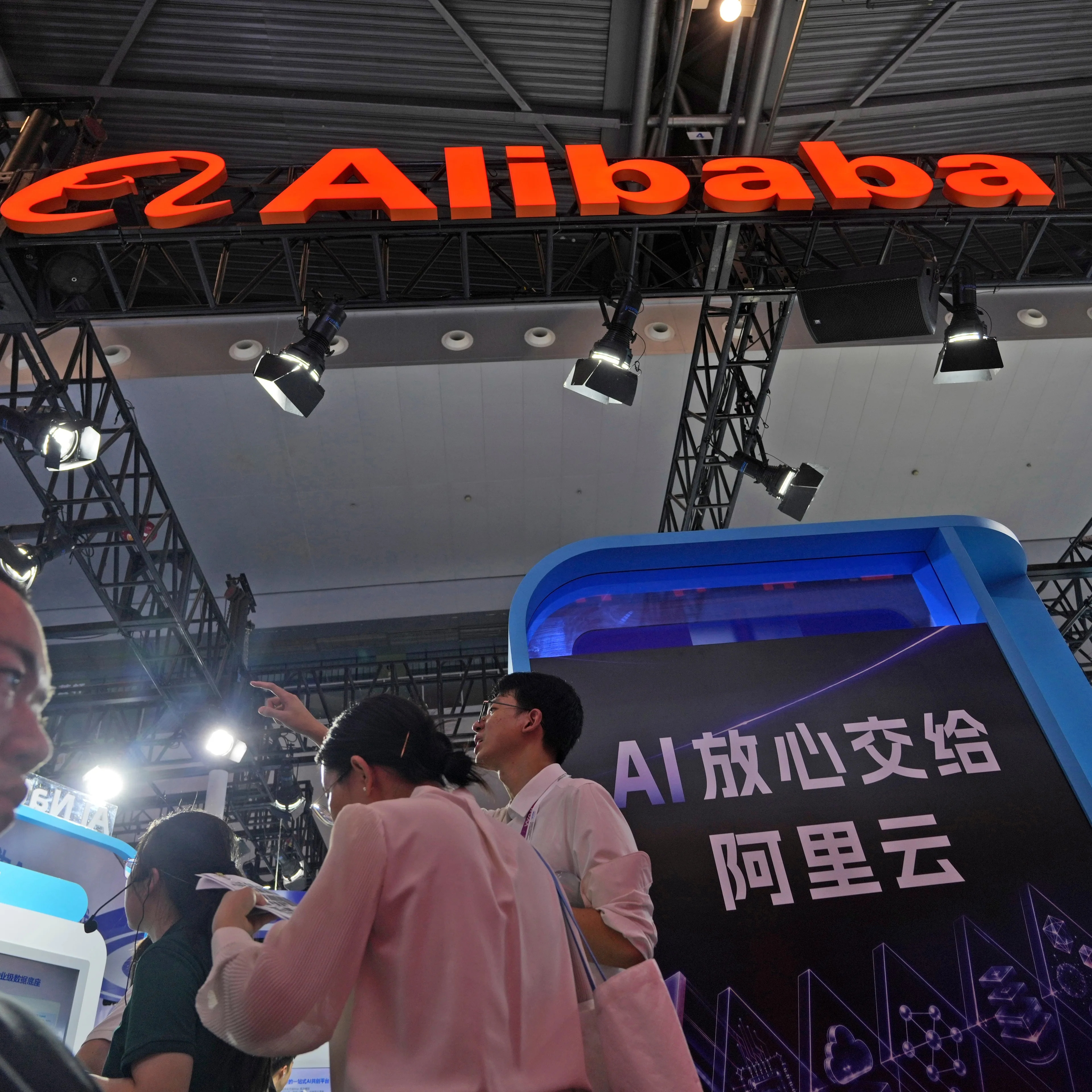 Alibaba-stand på teknologimesse med folk som ser på skjermer og informasjon om AI. (Bildebeskrivelsen er laget av en KI-tjeneste)