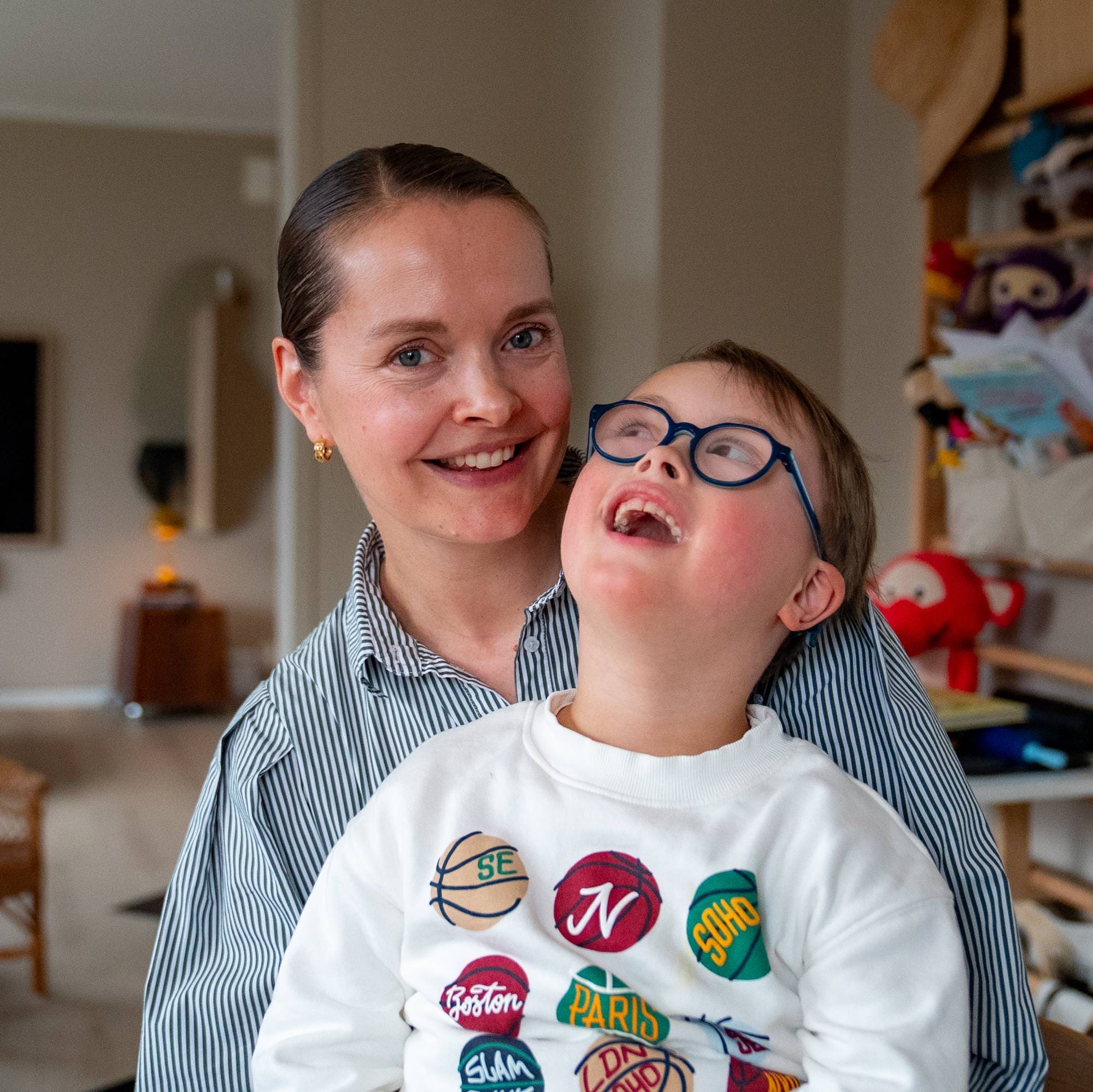 Gutt sitter på fanget til mor og ser opp mot henne. Begge smiler. 
