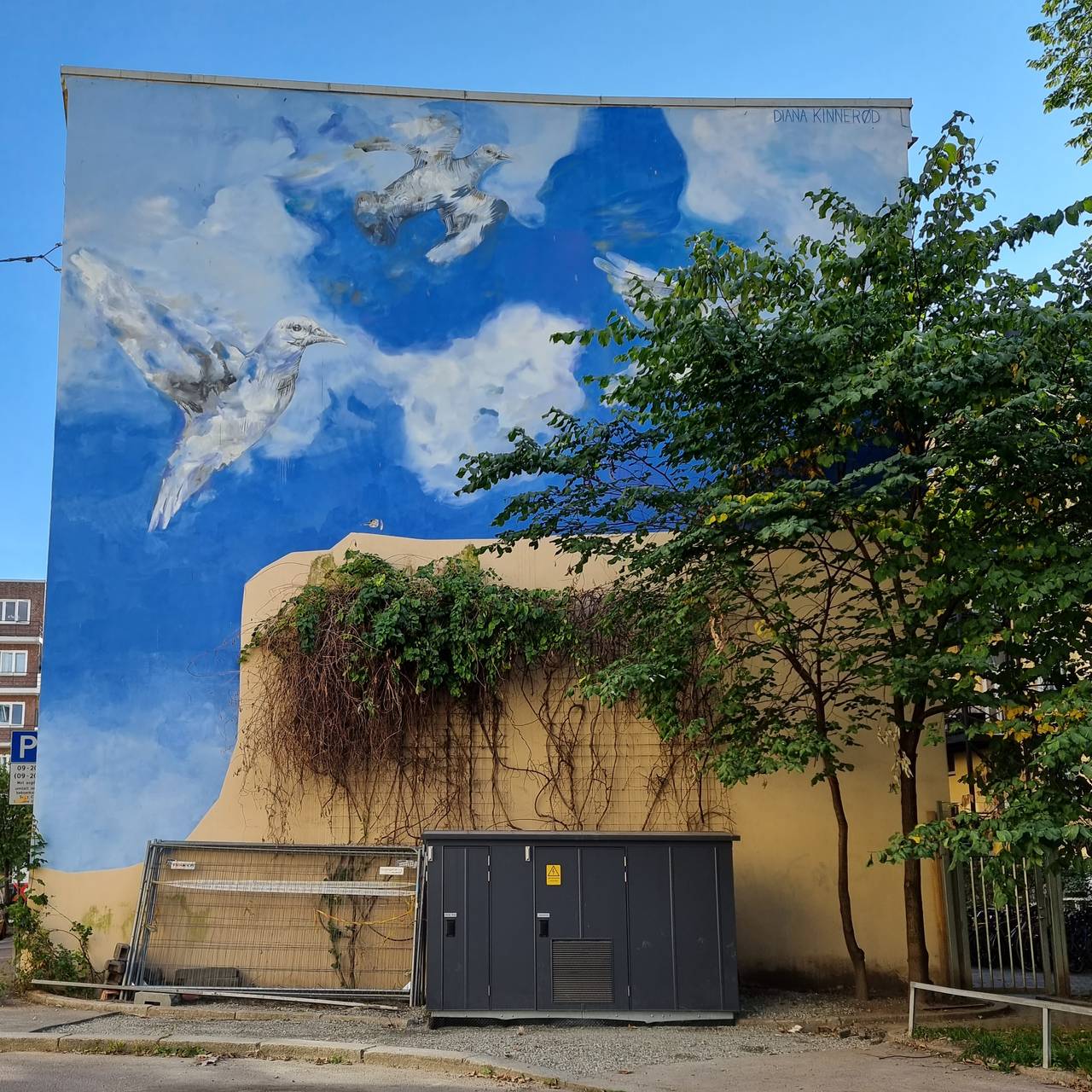 Diana Kinnerøds maleri av duer på blå himmel med skyer malt på gavlvegg på Tøyen.