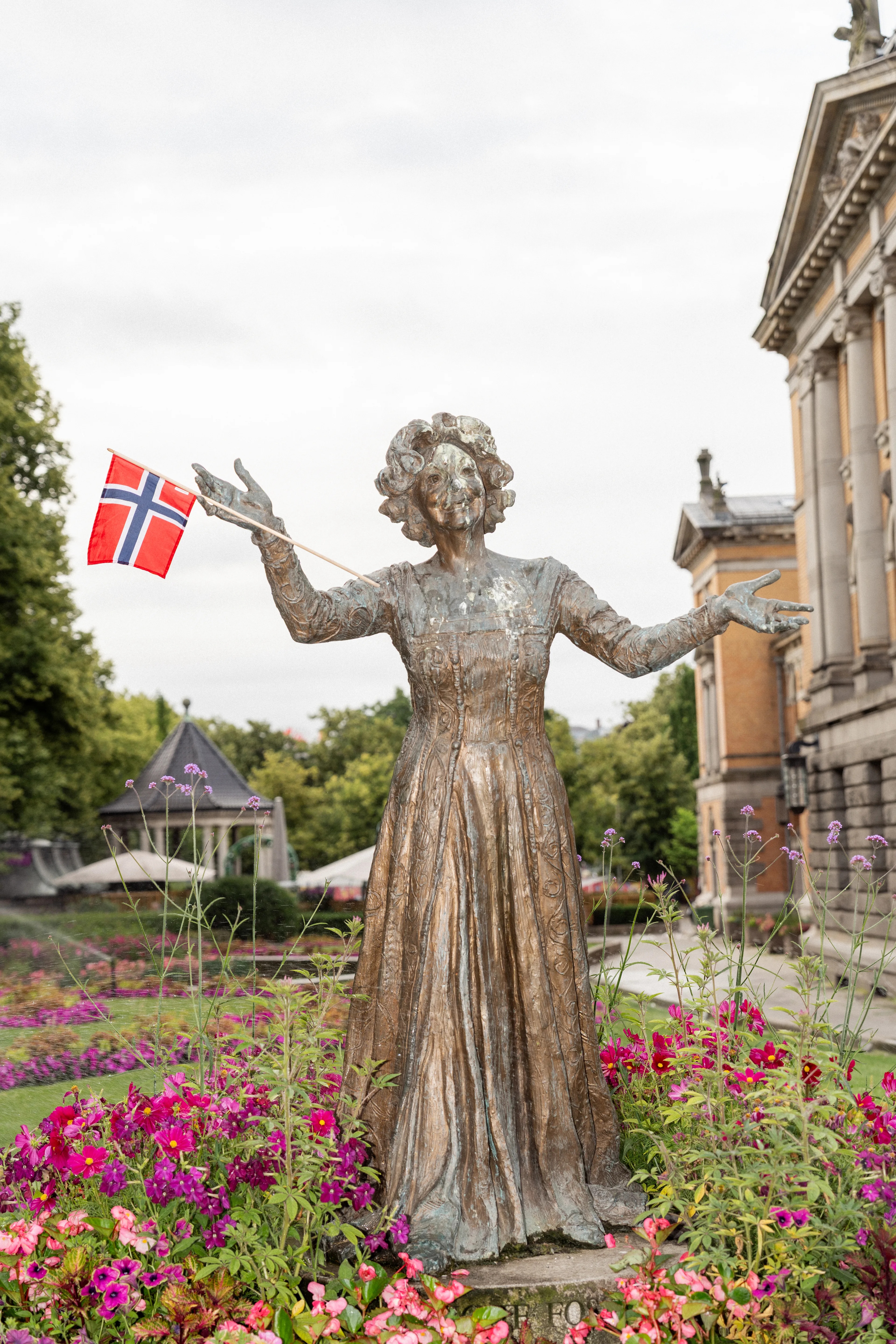 Bronzestatue av kvinne med norsk flagg i en park foran en bygning. (Bildebeskrivelsen er laget av en KI-tjeneste)