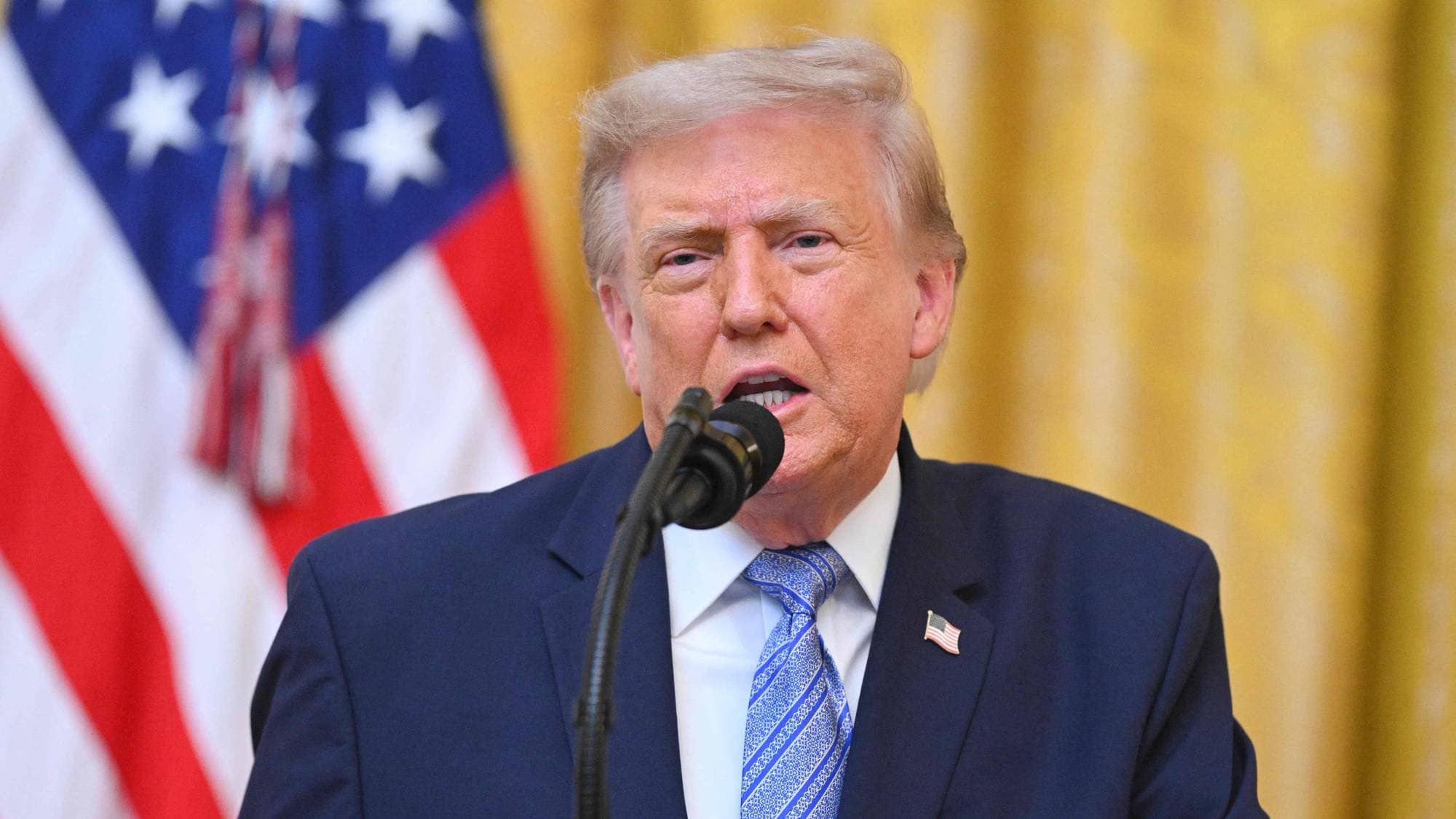Donald Trump snakker i en mikrofon foran et amerikansk flagg. (Bildebeskrivelsen er laget av en KI-tjeneste)